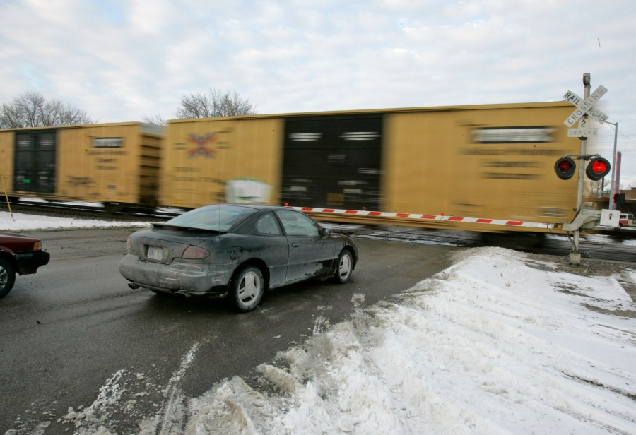 FILE - Cars wait for a train to pass, in Valley, Neb., Wednesday, Jan. 17, 2007. With the rail industry relying on longer and longer trains to cut costs, the Biden administration is handing out $570 million in grants to help eliminate railroad crossings in 32 states. The grants announced Monday, June 5, 2023 will help eliminate more than three dozen crossings that delay traffic and sometimes keep first responders from where help is desperately needed. (AP Photo/Nati Harnik, File)