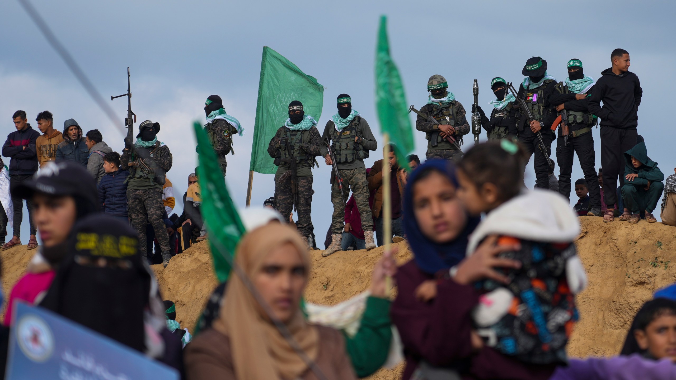 FILE - Palestinians watch as Hamas fighters take up a position ahead of handing over four bodies to the Red Cross in Khan Younis, southern Gaza Strip, Thursday, Feb. 20, 2025.(AP Photo/Abdel Kareem Hana, File)