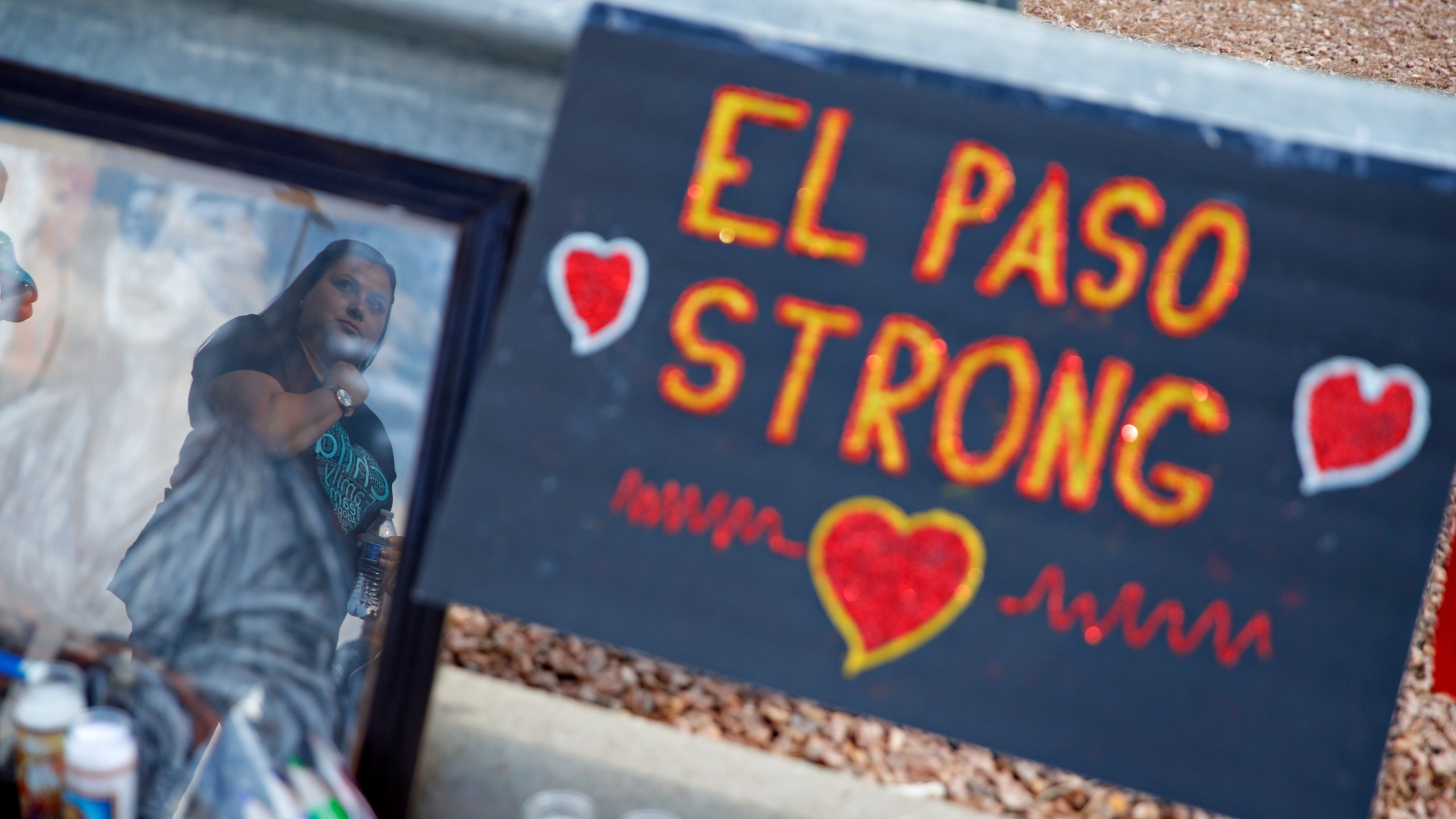 FILE - A woman is reflected in a picture as she looks at a makeshift memorial at the scene of a mass shooting at a shopping complex Tuesday, Aug. 6, 2019, in El Paso, Texas. (AP Photo/John Locher, File)