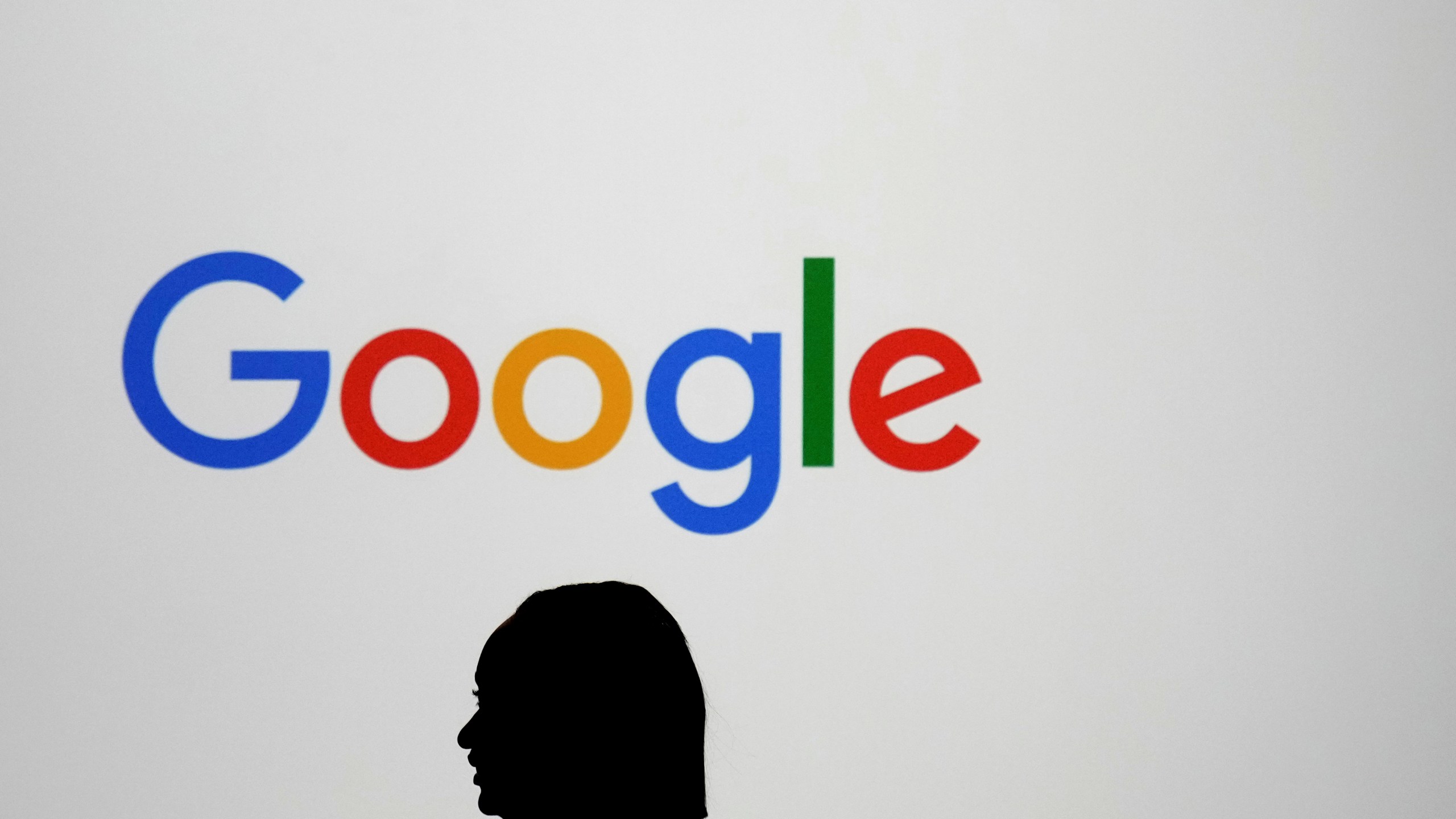 FILE - A woman walks by a giant screen with a logo at an event at the Paris Google Lab on the sidelines of the AI Action Summit in Paris, Sunday, Feb. 9, 2025. (AP Photo/Thibault Camus, File)