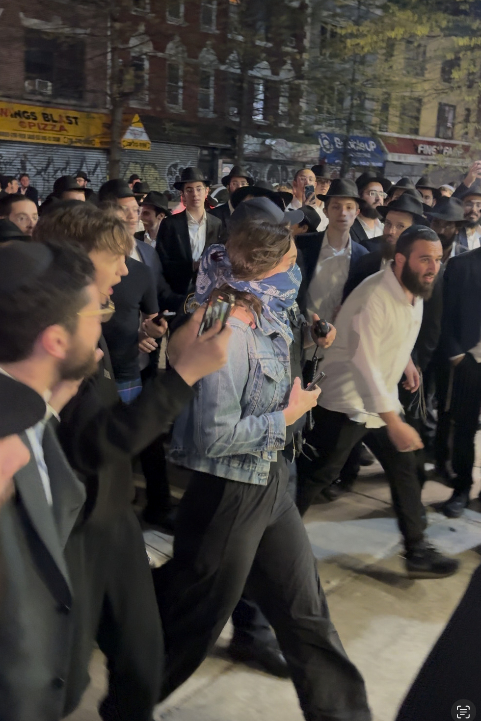 This image taken from video shows a woman and a police officer as they are pursued by a crowd of men in the Crown Heights section of Brooklyn, N.Y., on Thursday, April 24, 2025. (AP Photo)