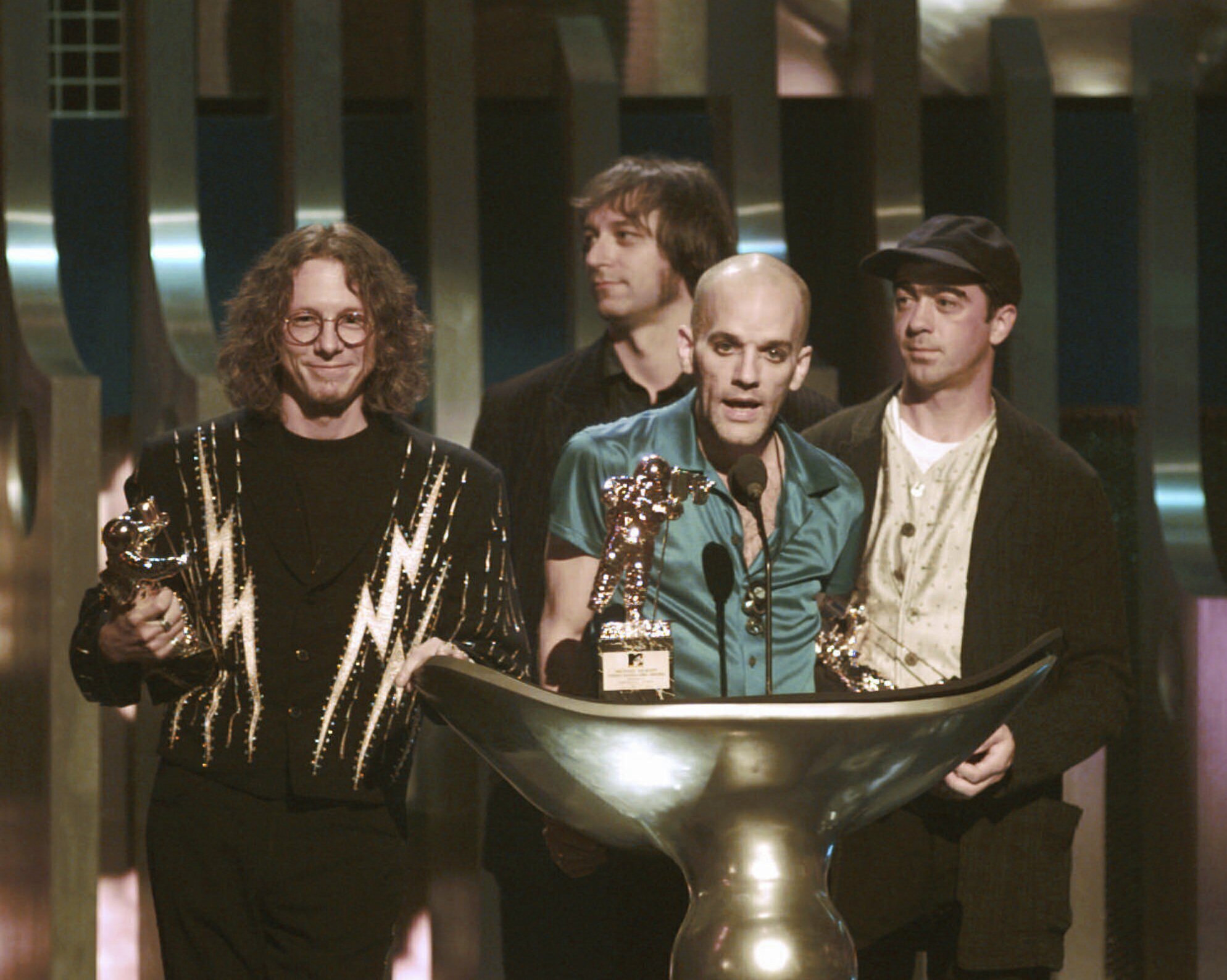 FILE - Michael Stipe, of the band R.E.M., center, speaks as he accepts the Video Vanguard award during the 1995 MTV Video Music Awards at Radio City Music Hall in New York on Sept. 7, 1995. Standing by are fellow band members, from left, Mike Mills, Peter buck and Bill Berry. (AP Photo/Bebeto Matthews, File)