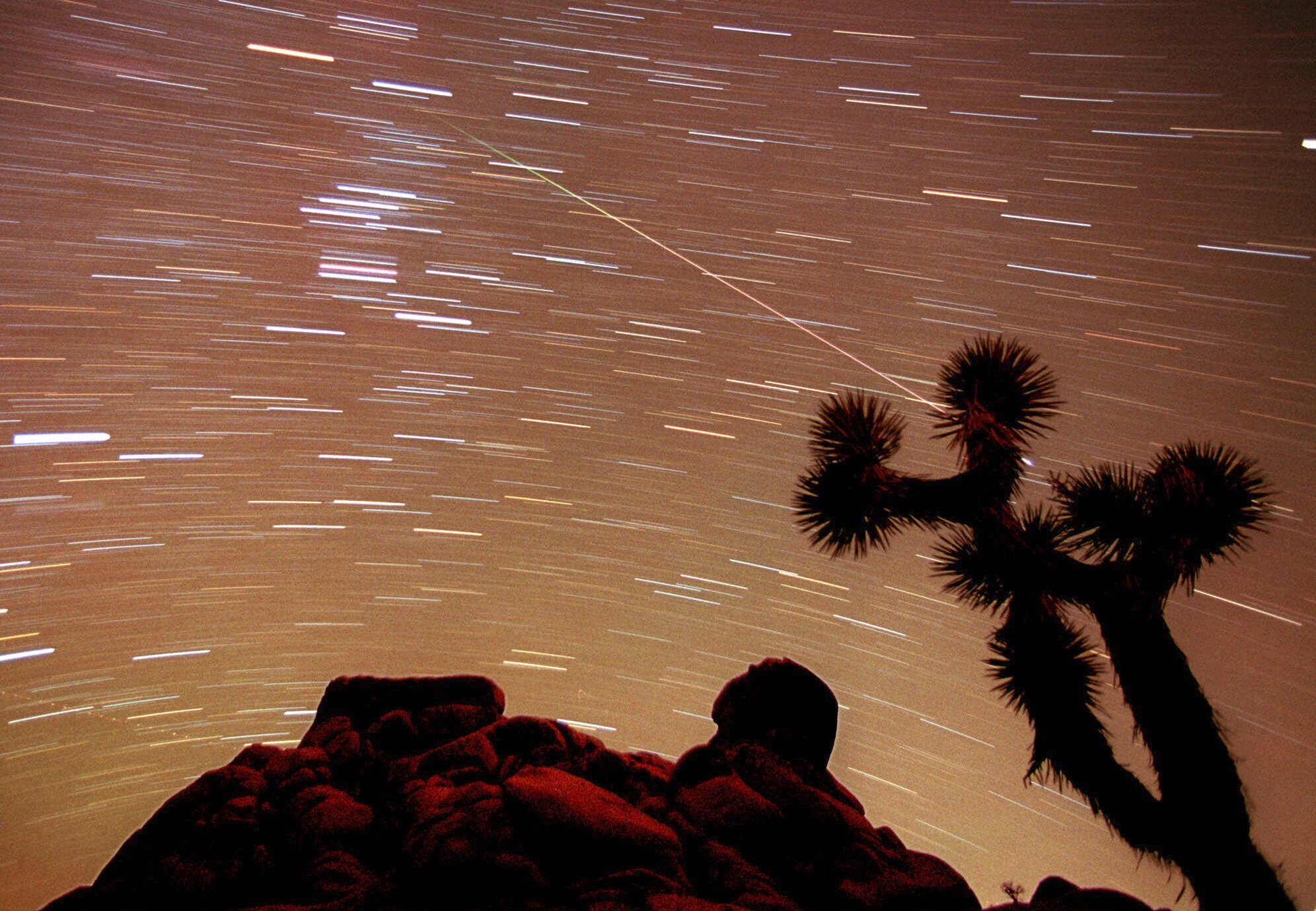 FILE - A meteor streaks through the sky over Joshua trees and rocks at Joshua Tree National Park in Southern California's Mojave Desert in this 30-minute time exposure ending at 1:15 a.m. PST, Nov. 17, 1998. Stars moving through the sky as the Earth rotates are seen as a series of short lines across the frame. (AP Photo/Reed Saxon, File)