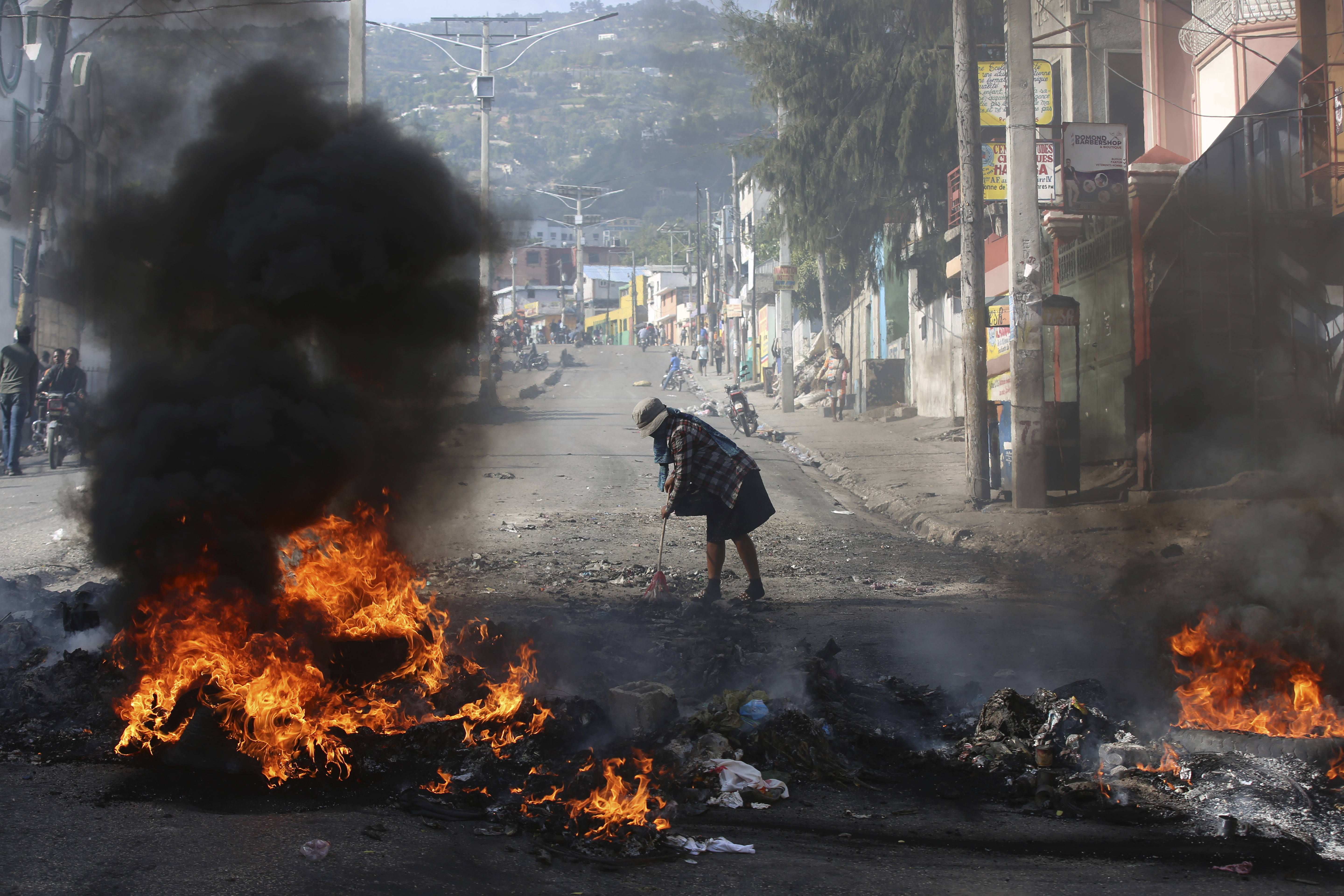A woman sweeps debris next to a blazing barricade set up by demonstrators during a protest against insecurity in Port-au-Prince, Haiti, Wednesday, April 2, 2025. (AP Photo/Odelyn Joseph)
