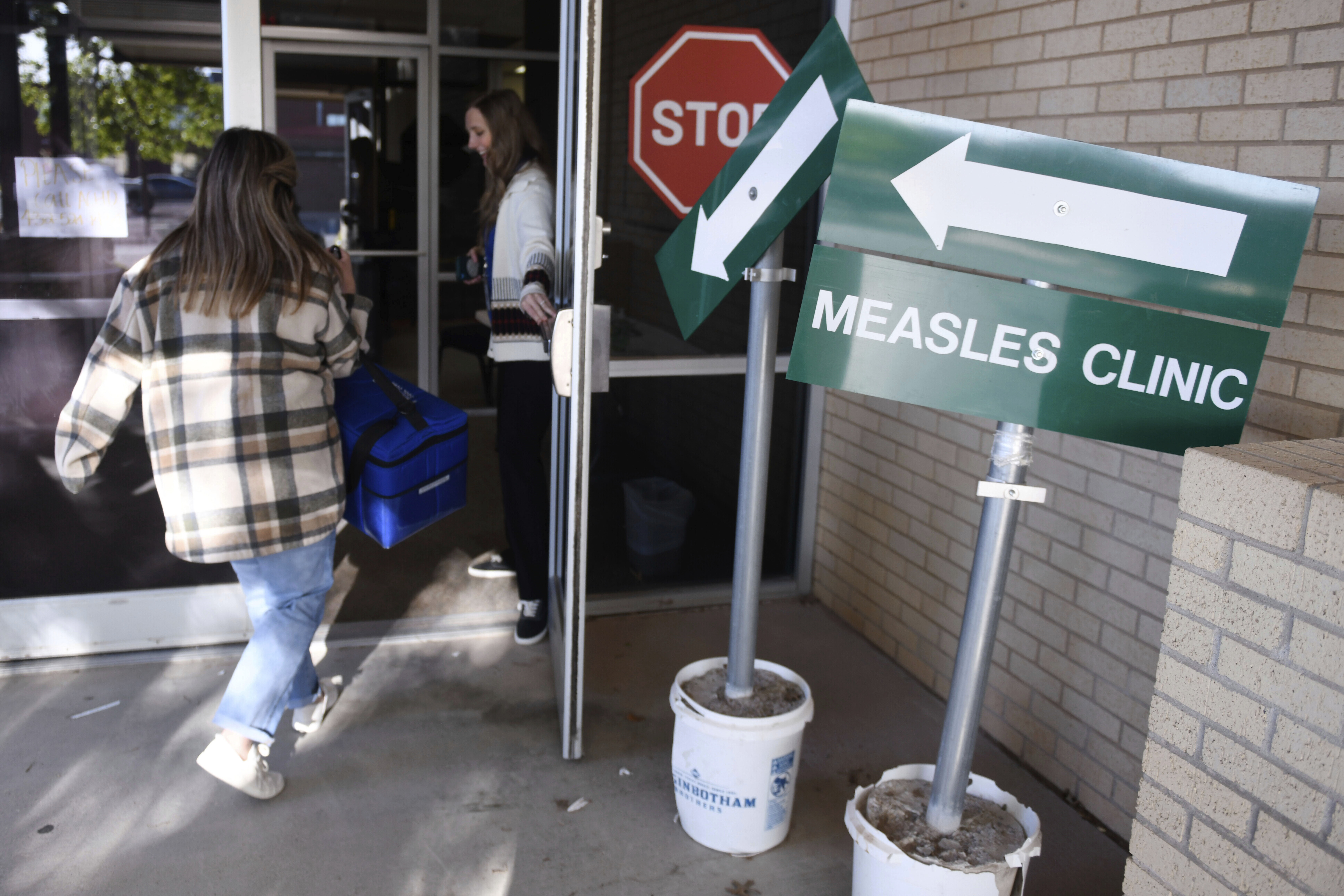 Health department staff members enter the Andrews County Health Department measles clinic carrying doses of the measles, mumps and rubella vaccine, Tuesday, April 8, 2025, in Andrews, Texas. (AP Photo/Annie Rice)