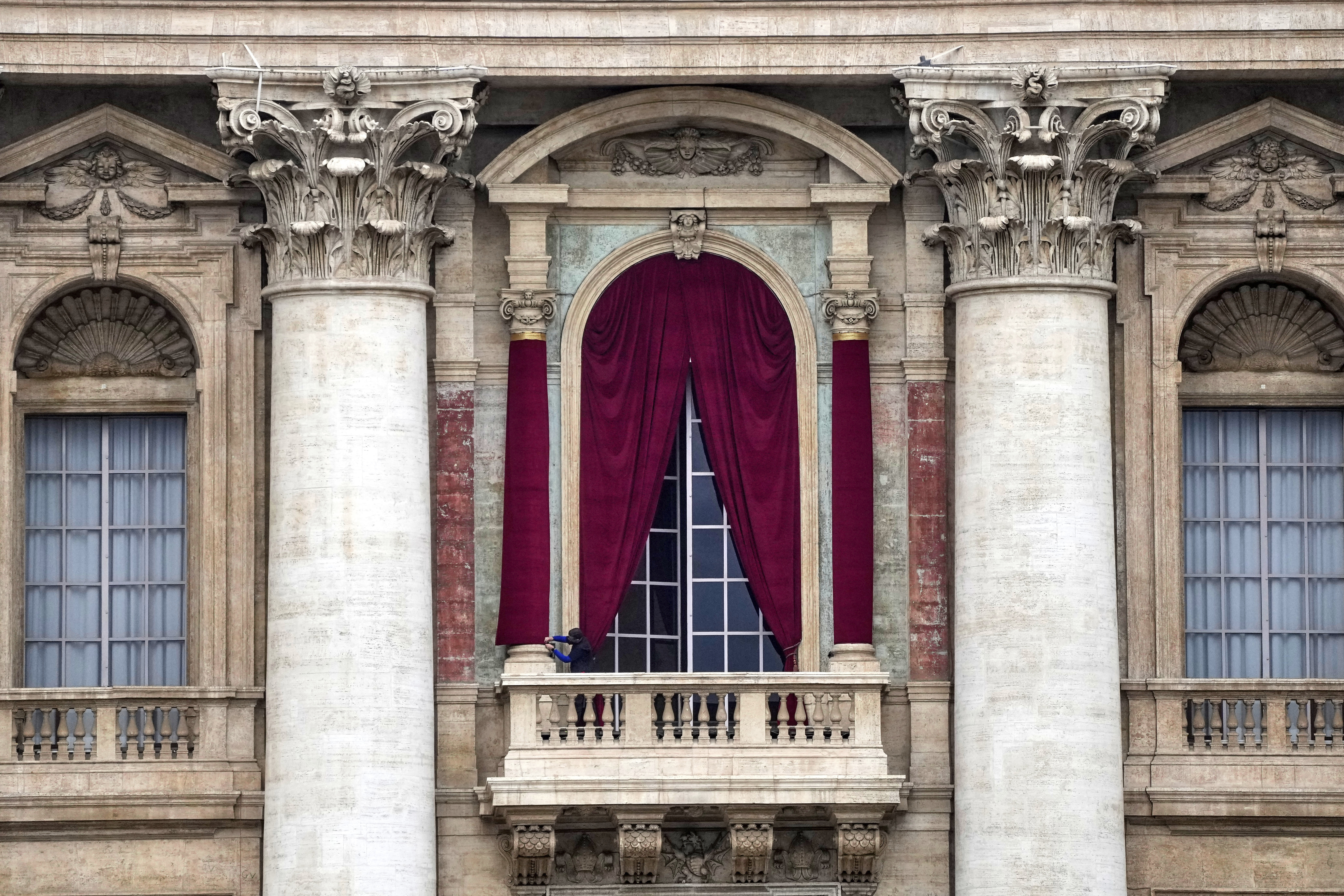 A man gives the last touch to a red drape wrapped around a column of the central lodge of St. Peter's Basilica in Vatican City, Monday, May 5, 2025, before the conclave starting on May 7, where they will elect the 267th pontiff of the Catholic Church. (AP Photo/Gregorio Borgia)
