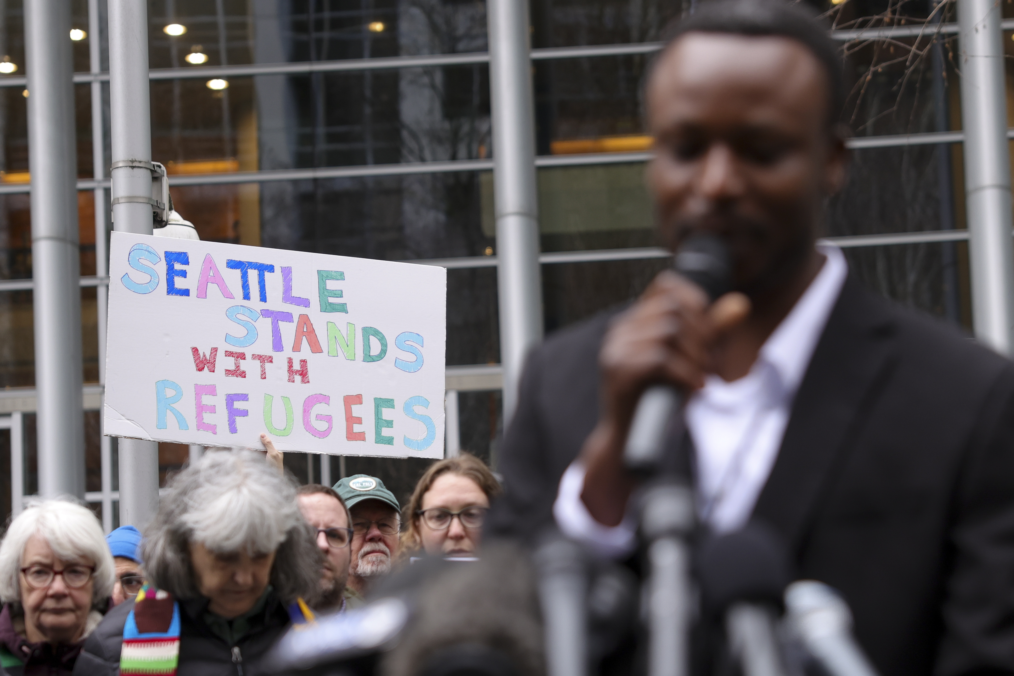 FILE - Signs are seen as Tshishiku Henry, a former refugee and Washington State Delegate for the Refugee Congress, speaks during a rally outside the U.S District Court after a federal judge blocked President Donald Trump's effort to halt the nation's refugee admissions system, Feb. 25, 2025 in Seattle. (AP Photo/Ryan Sun, File)