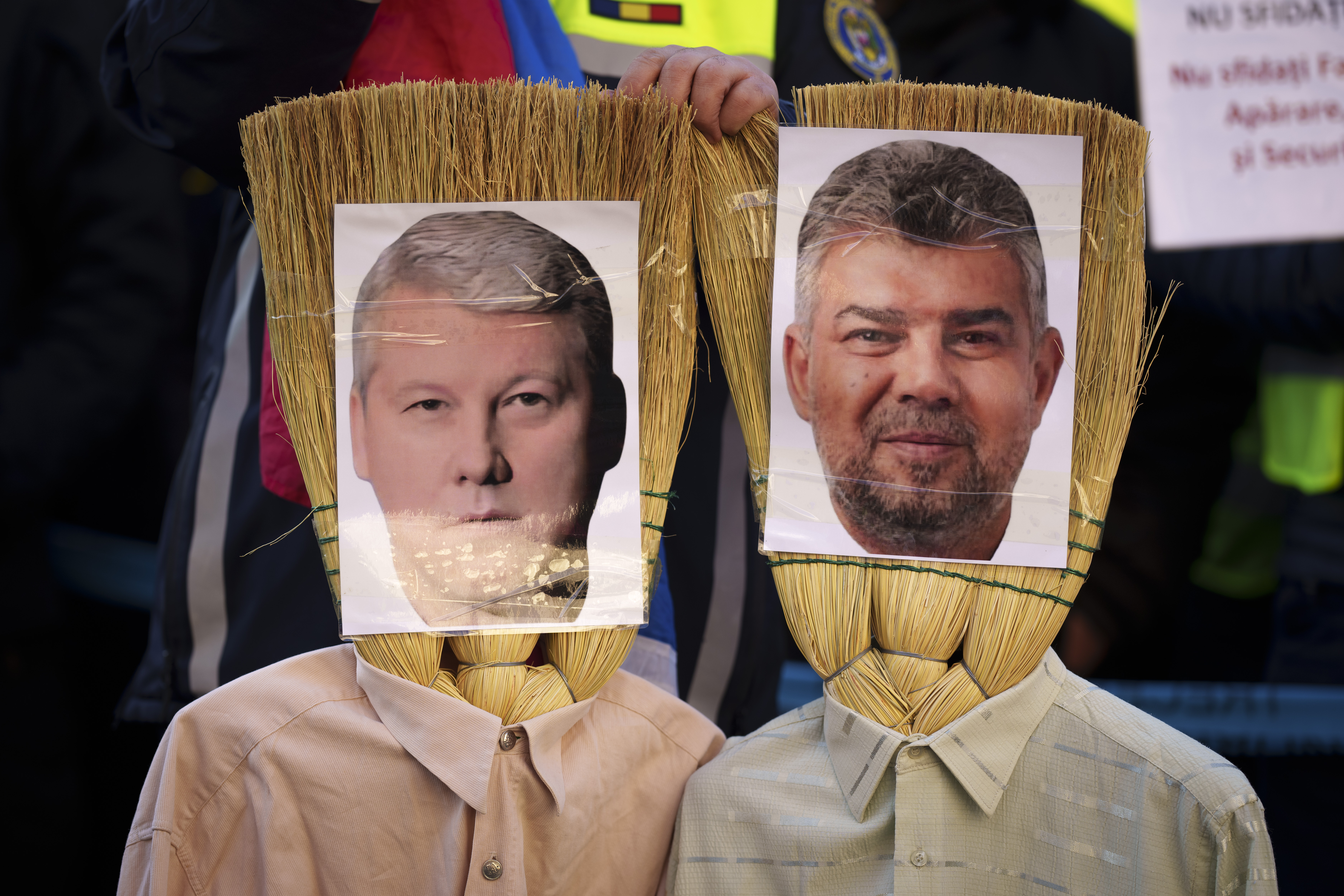 FILE - A Romanian policeman holds effigies made of brooms of Prime Minister Marcel Ciolacu, right, and Interior Minister Catalin Predoiu, left, during a protest in Bucharest, Romania, Jan. 17, 2025. (AP Photo/Vadim Ghirda, File)