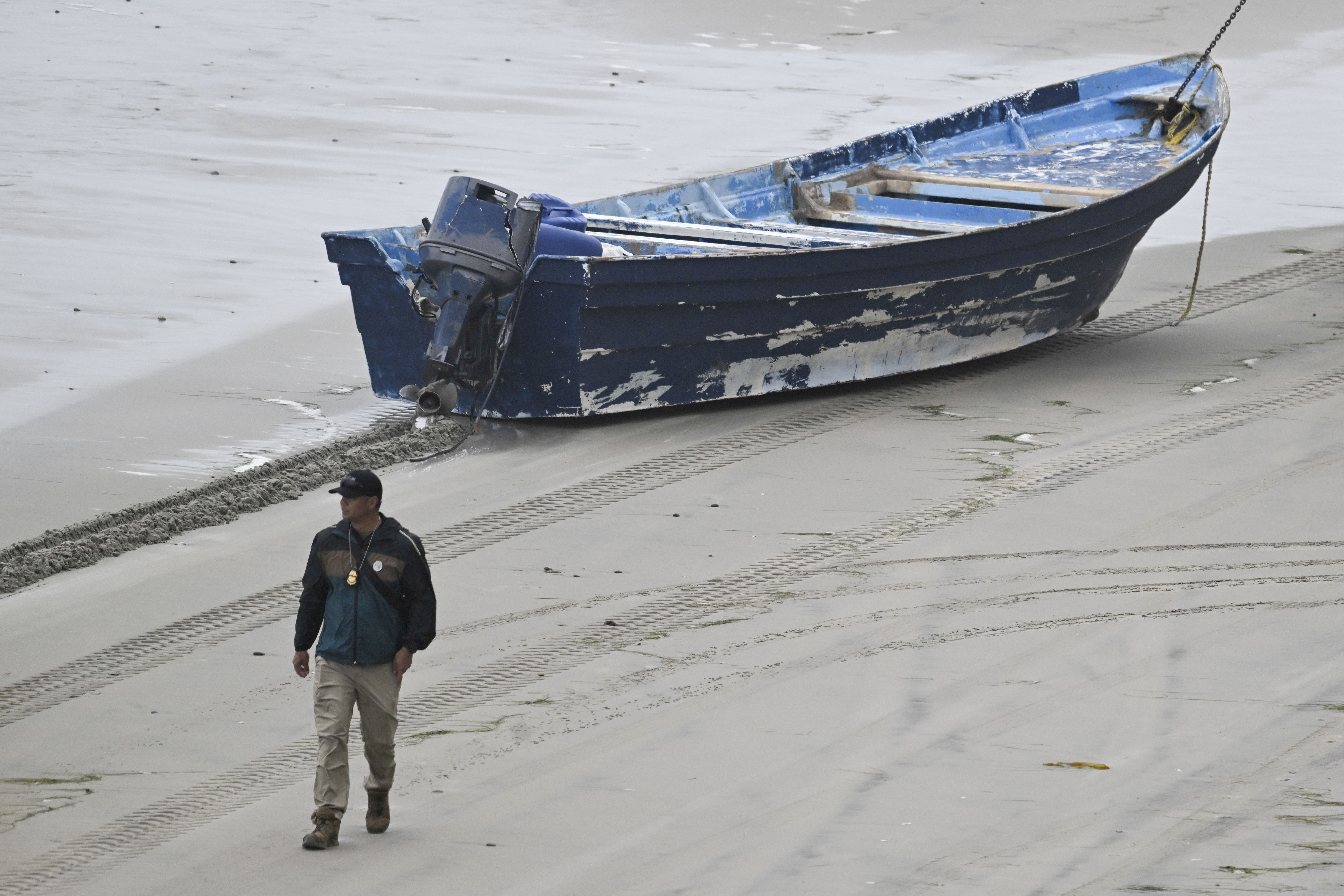 A law enforcement officer walks past capsized boat on the beach Monday, May 5, 2025, in at Torrey Pines State beach in San Diego, Calif. (AP Photo/Denis Poroy)