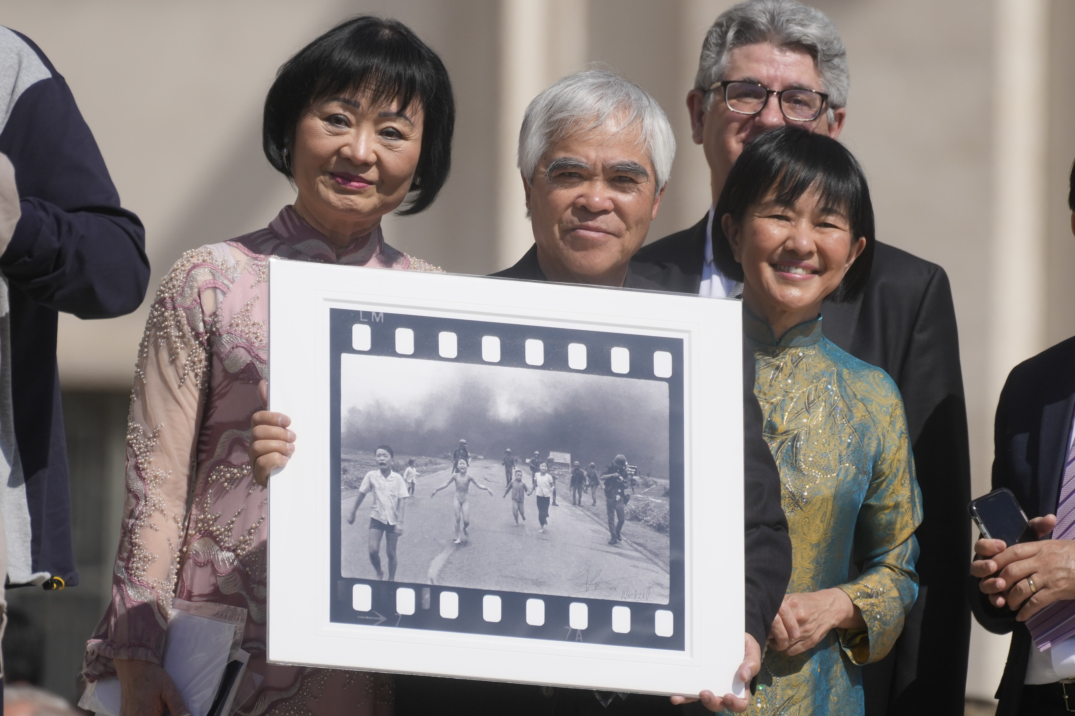 FILE - Pulitzer Prize-winning photographer Nick Ut, center, flanked by Kim Phuc, left, holds the" Napalm Girl", his Pulitzer Prize winning photo as they wait to meet with Pope Francis during the weekly general audience in St. Peter's Square at The Vatican, May 11, 2022. (AP Photo/Gregorio Borgia, file)