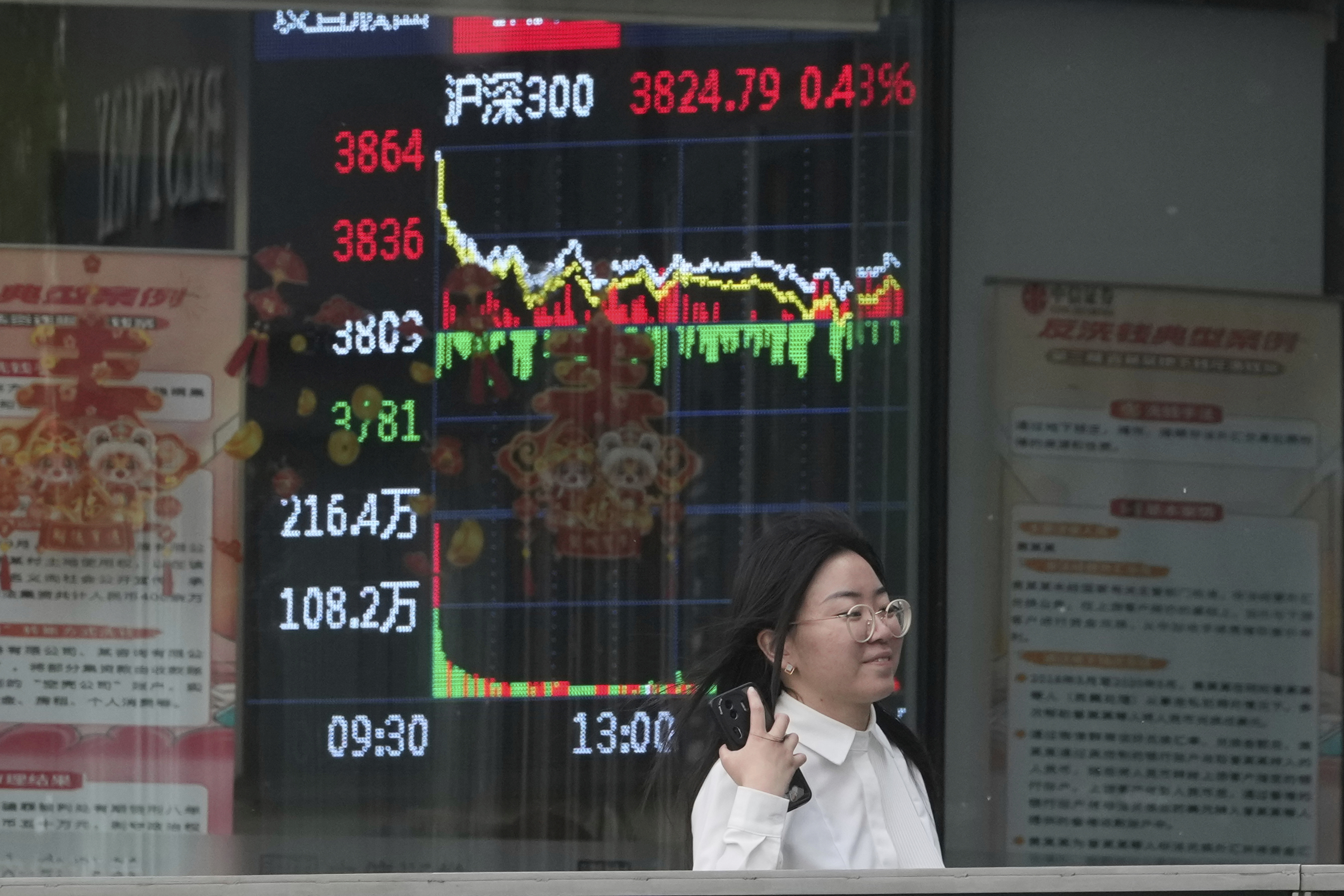 A woman passes by a stock index at a brokerage in Beijing, Wednesday, May 7, 2025. (AP Photo/Ng Han Guan)