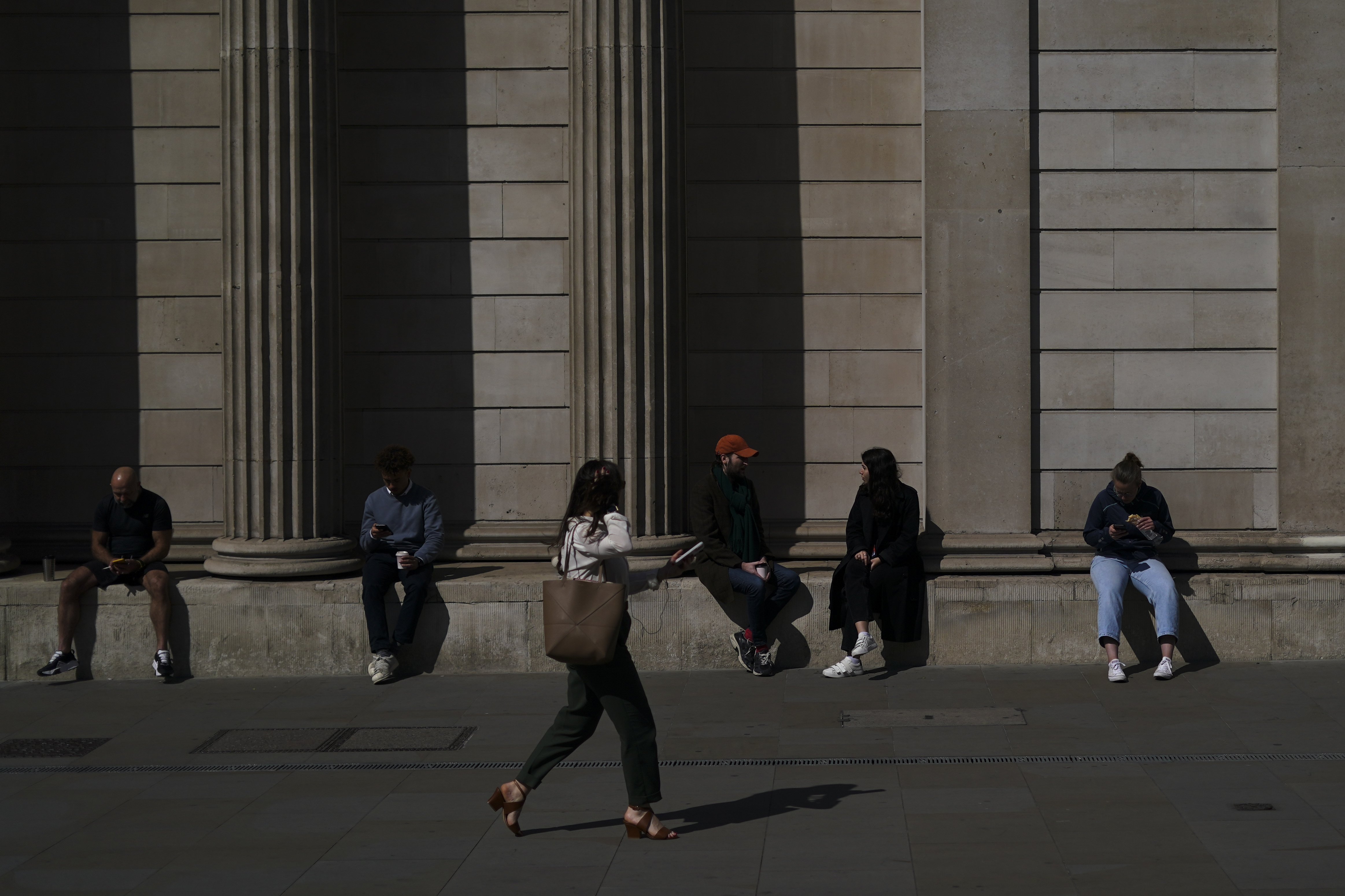 People sit on the wall of the Bank of England in the financial district known as The City, in London, Wednesday, April 9, 2025.(AP Photo/Alberto Pezzali)