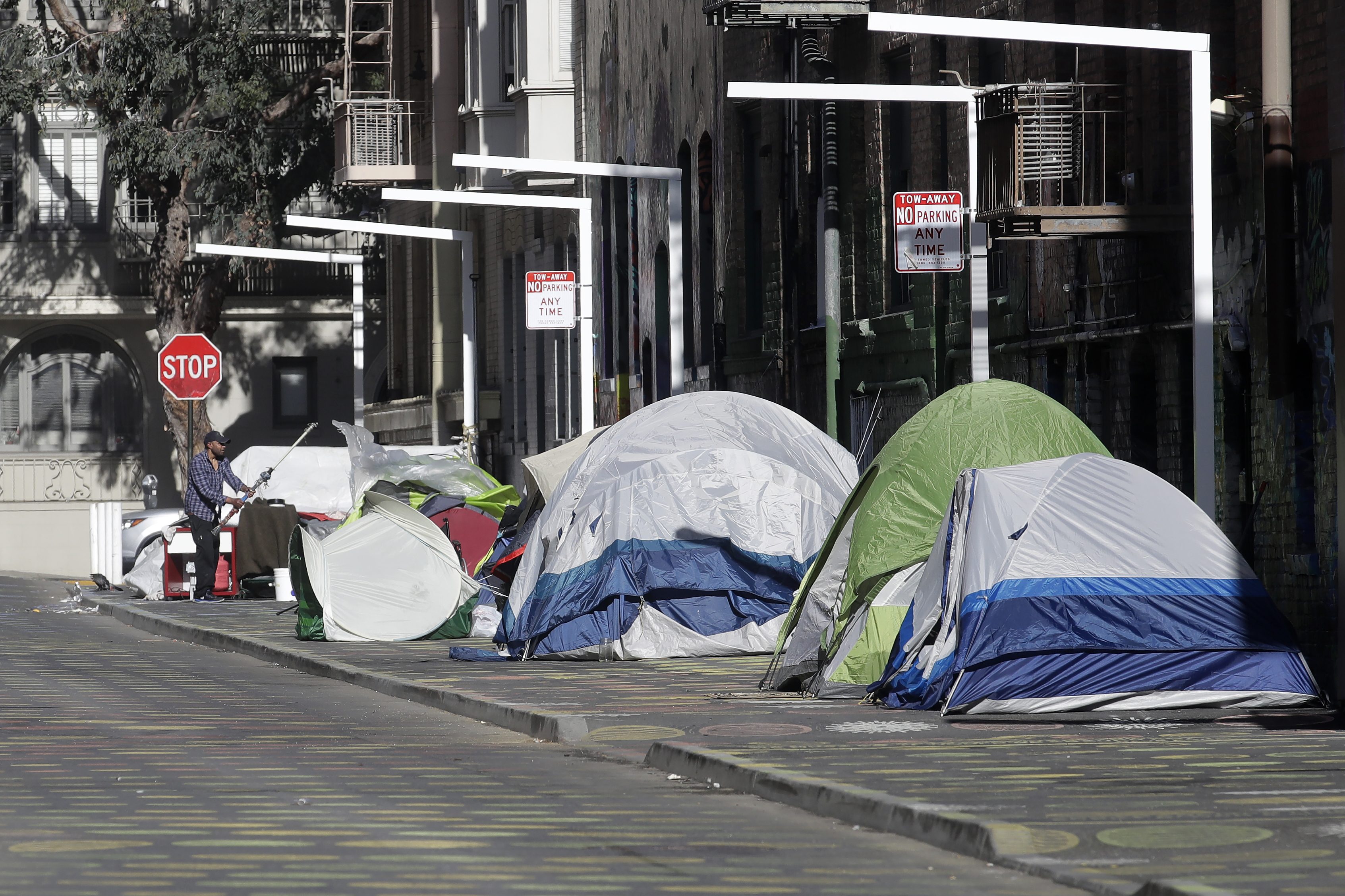 FILE - A man stands next to tents on a sidewalk in San Francisco on April 21, 2020. (AP Photo/Jeff Chiu, File)