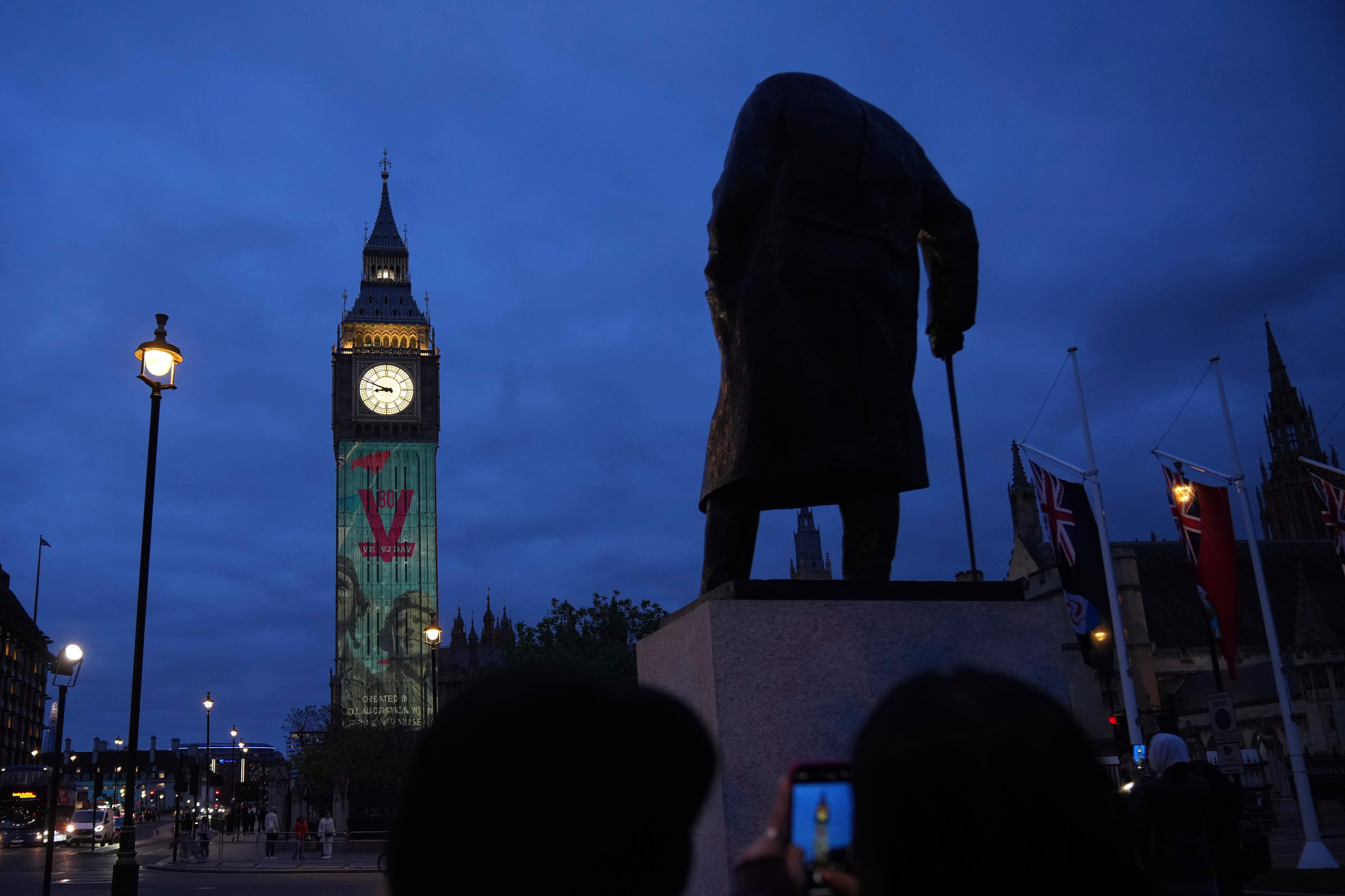 Images are projected onto the Queen Elizabeth Tower, in the Houses of Parliament, including the British World War II Prime Minister Winston Churchill, whose statue is in the foreground, during the V-E Day 80th anniversary events in London, Tuesday, May 6, 2025. (AP Photo/Alastair Grant)