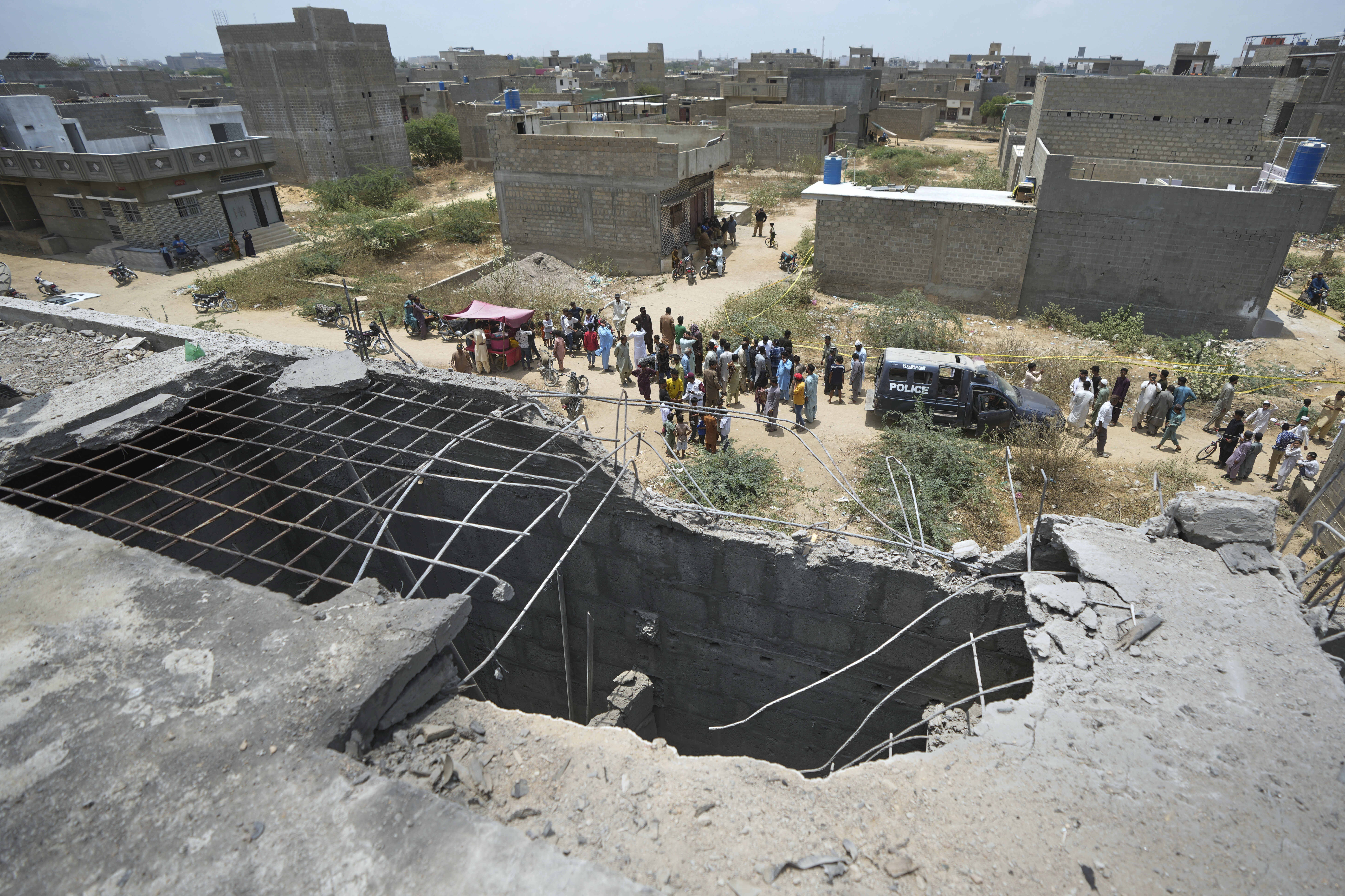 A big hole is seen on a rooftop of a house suspected to have been damaged in Indian drone attack as residents, behind, gather near a cordoned off site, where Pakistan's air defense system shot down a suspected Indian drone in Karachi, Pakistan, Thursday, May 8, 2025. (AP Photo/Fareed Khan)