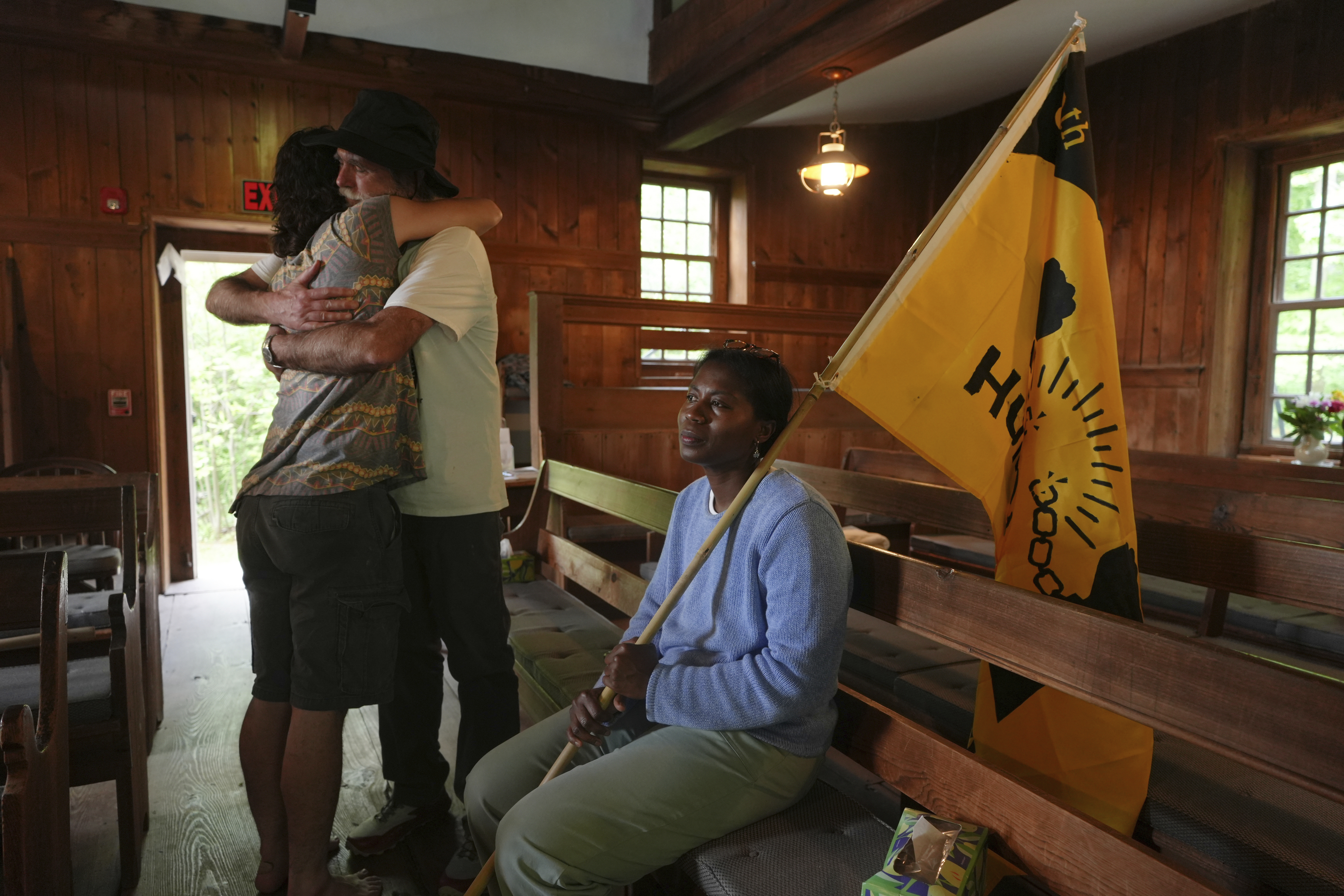 Casey Oware, a member of the Princeton Friends Meeting, seated, holds a flag while Stuart Sydenstricker, right, and Jules Wing Vasquez hug after completing a portion of the Quaker March to Washington at the Quaker Meeting House in Princeton, N.J. (AP Photo/Luis Andres Henao)