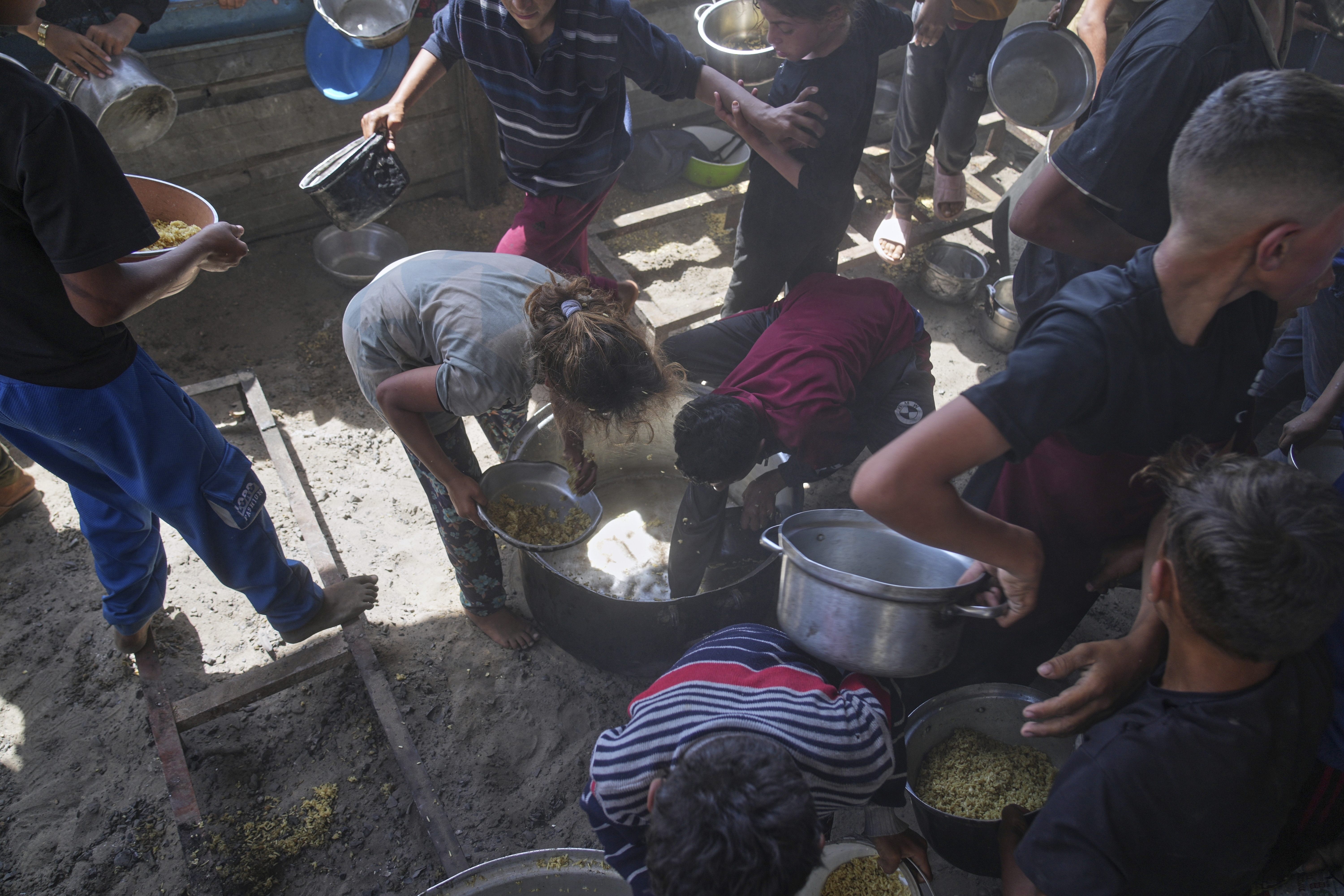 Palestinian children scrape a pot for leftover food after all meals were distributed at a community kitchen in Khan Younis, southern Gaza Strip, on Friday, May 9, 2025.