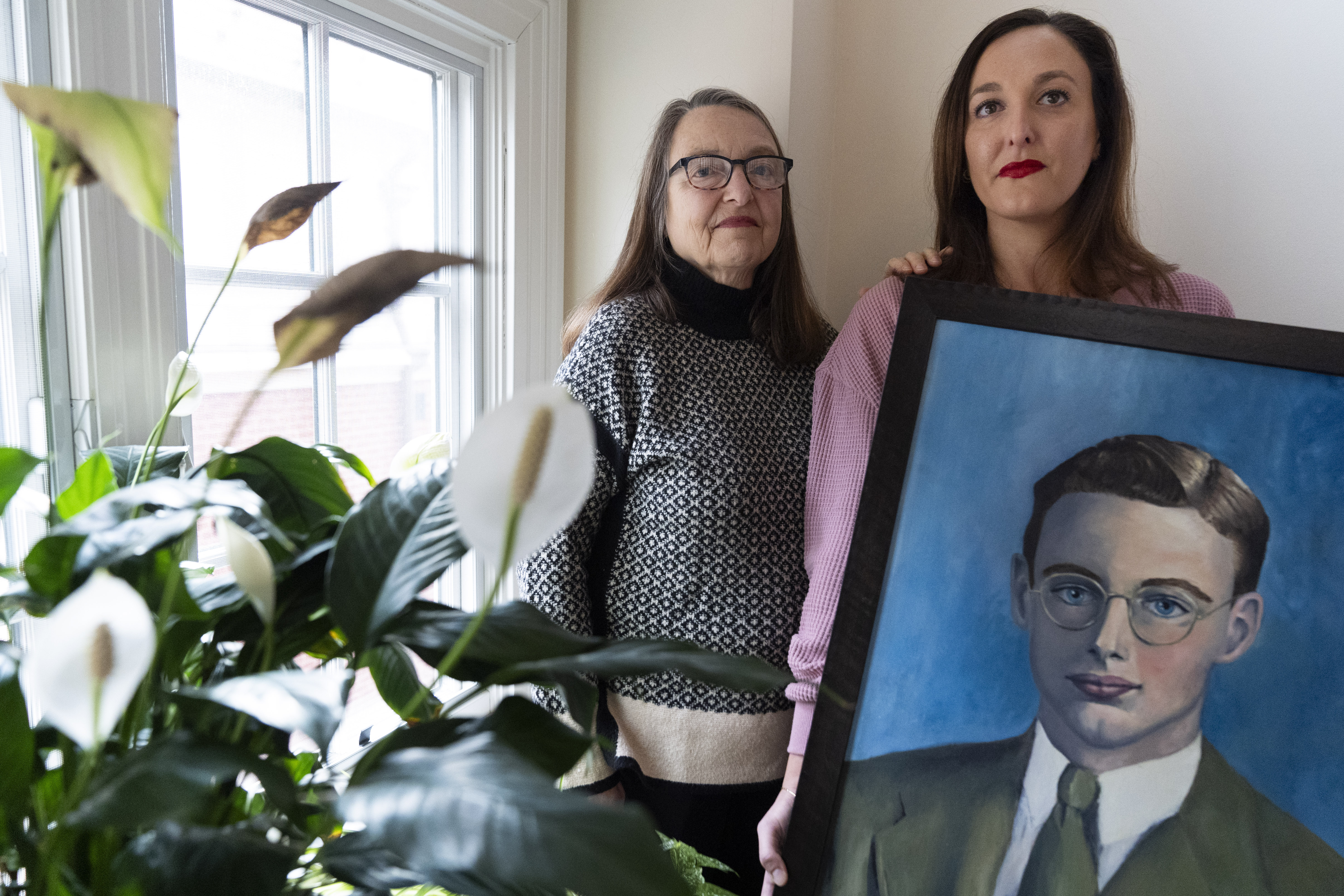 Cathy Votaw, 69, left, and her daughter Anna Eisenberg, pose with a painting of Votaw's father, Albert Votaw, portrayed as a young man in the 1940's, Thursday, Feb. 27, 2025, at their home in Washington. (AP Photo/Jacquelyn Martin)
