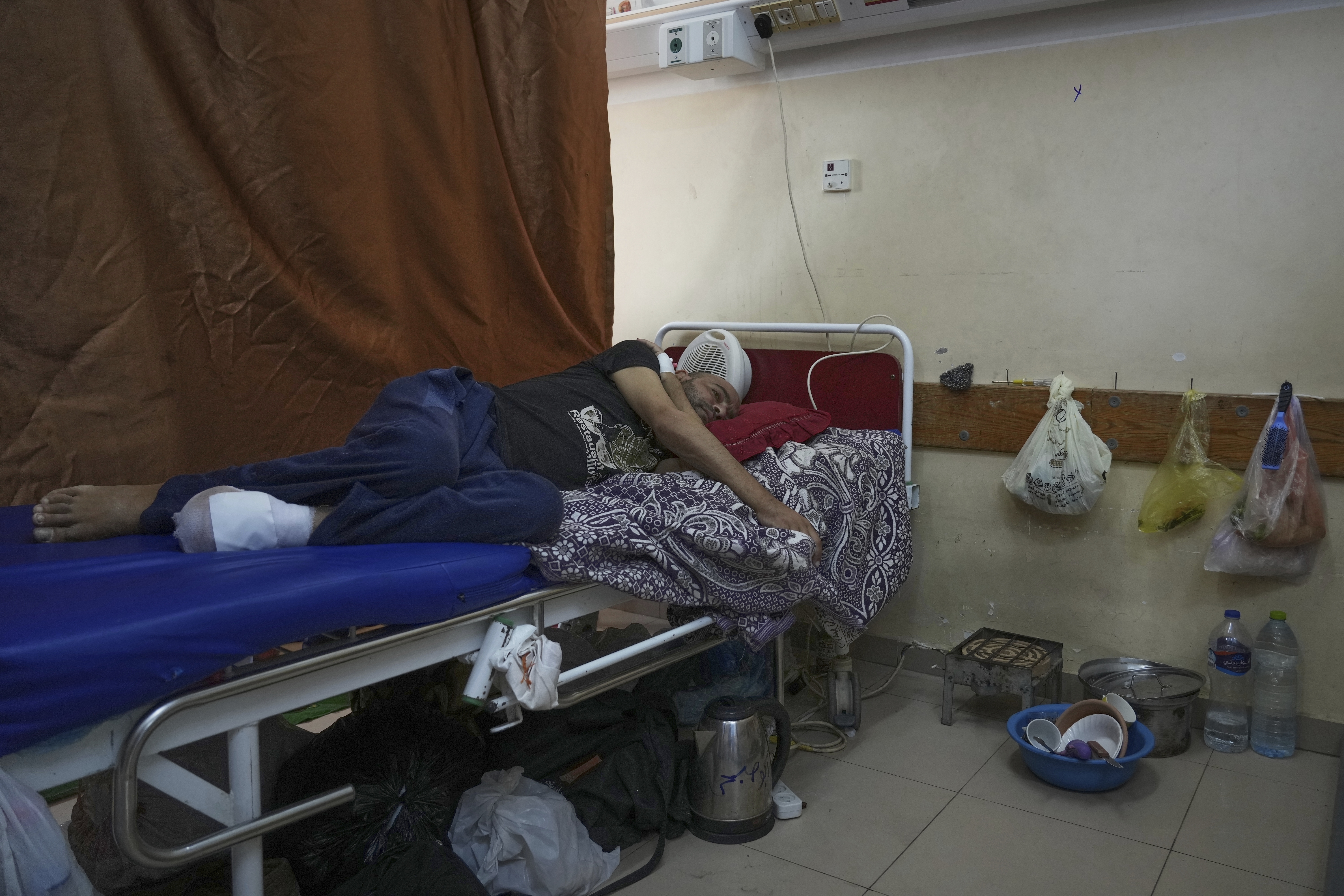Sobhi al-Bursh, who was injured in a bombing and lost his foot, lies in bed next to dishes and a portable electric stove used to cook food brought from home at Nasser Hospital in Khan Younis, Gaza Strip, Tuesday, May 6, 2025. (AP Photo/Abdel Kareem Hana)