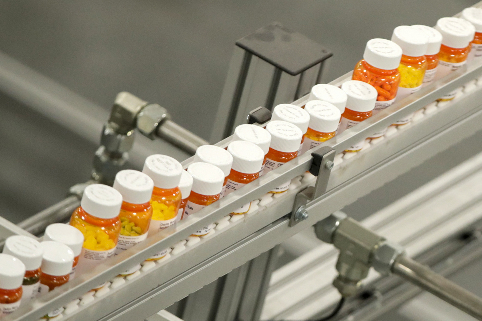 FILE- Bottles of medicine ride on a belt at a mail-in pharmacy warehouse in Florence, N.J., July 10, 2018. President Donald Trump’s plan to change the pricing model for some medications is facing fierce criticism from the pharmaceutical industry before he’s even signed an executive order he says will lower the costs of drugs. (AP Photo/Julio Cortez, File)