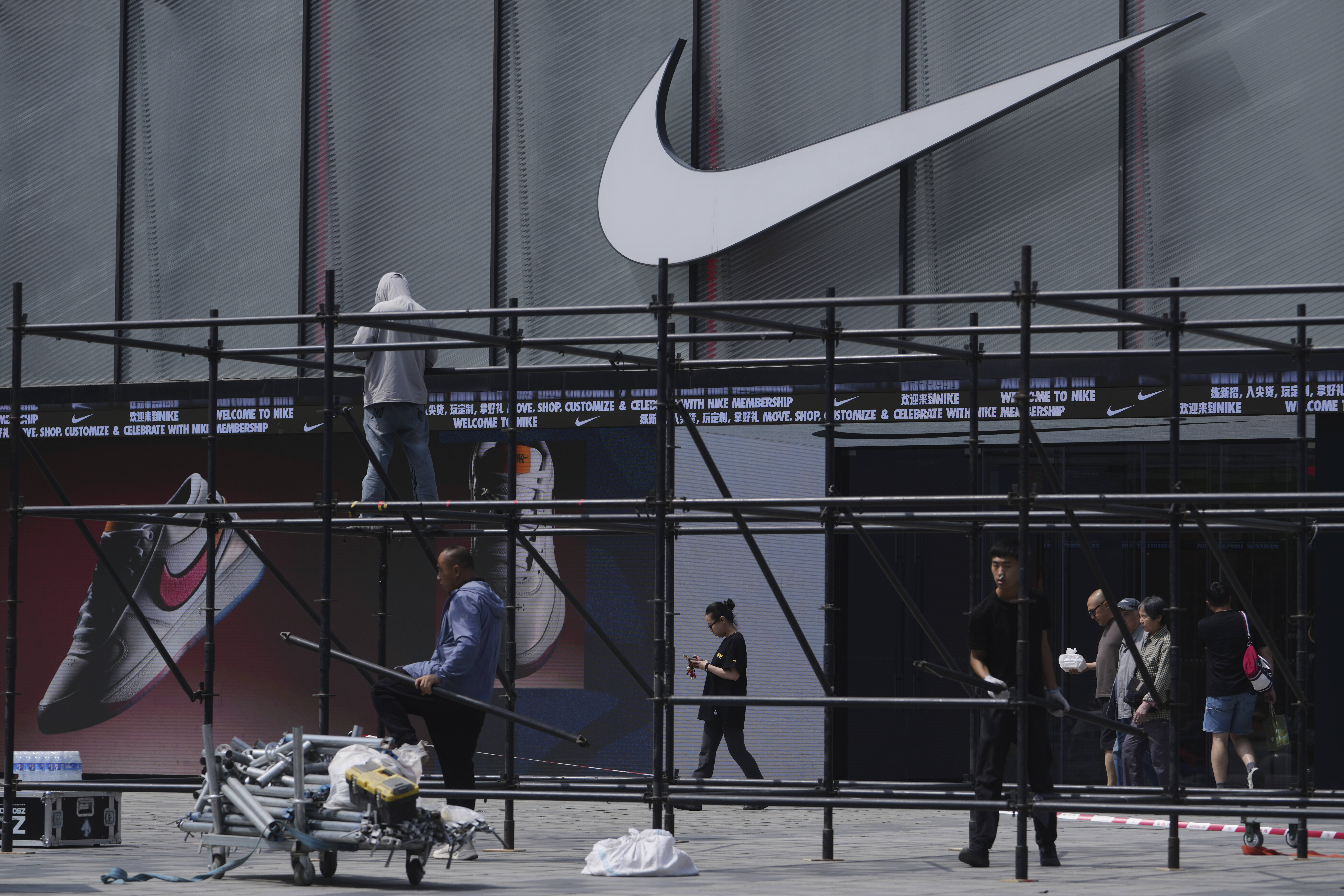Shoppers walk by as workers install a platform near a Nike store outside a shopping mall in Beijing, Sunday, May 11, 2025. (AP Photo/Andy Wong)