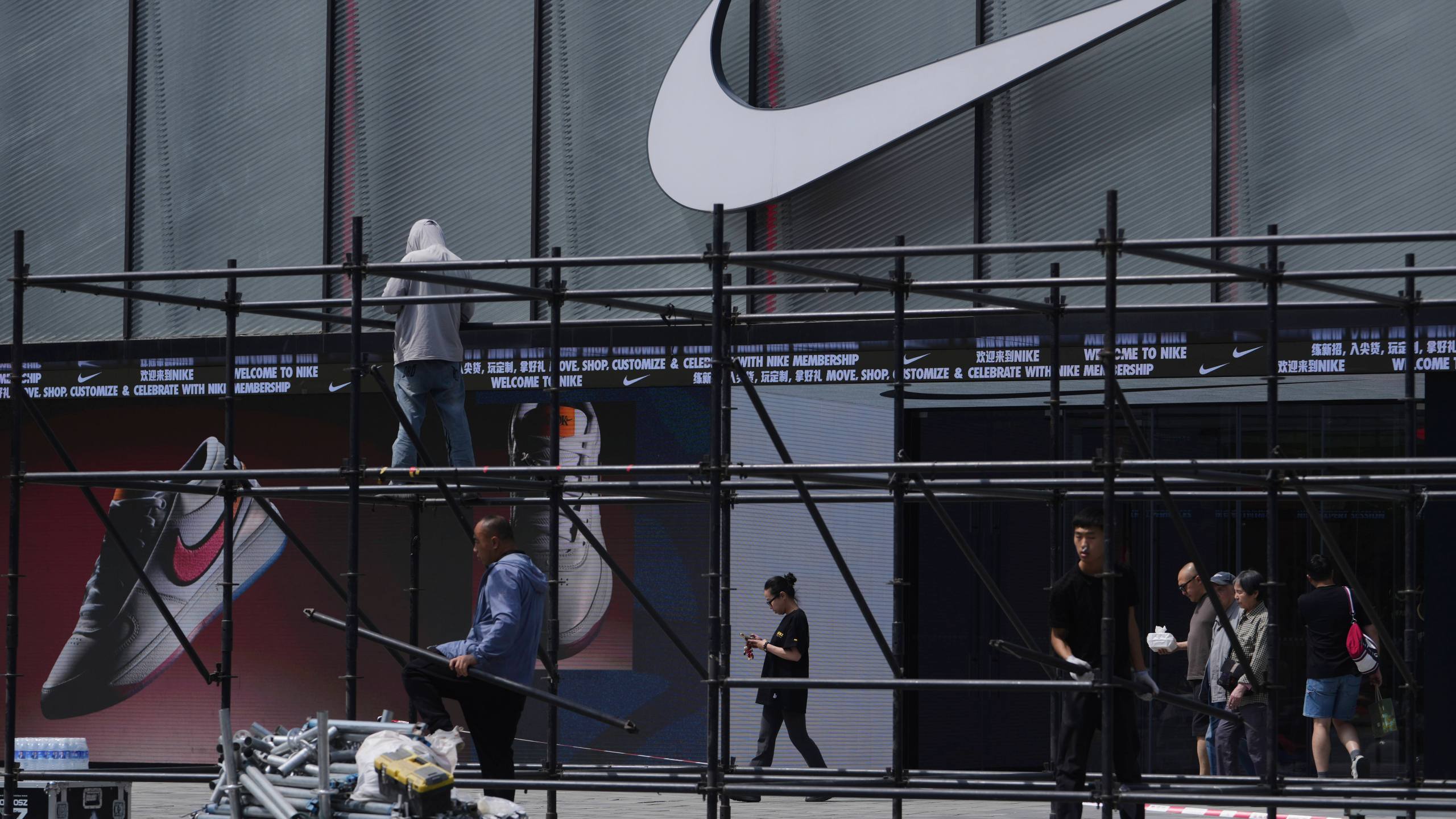 Shoppers walk by as workers install a platform near a Nike store outside a shopping mall in Beijing, Sunday, May 11, 2025. (AP Photo/Andy Wong)