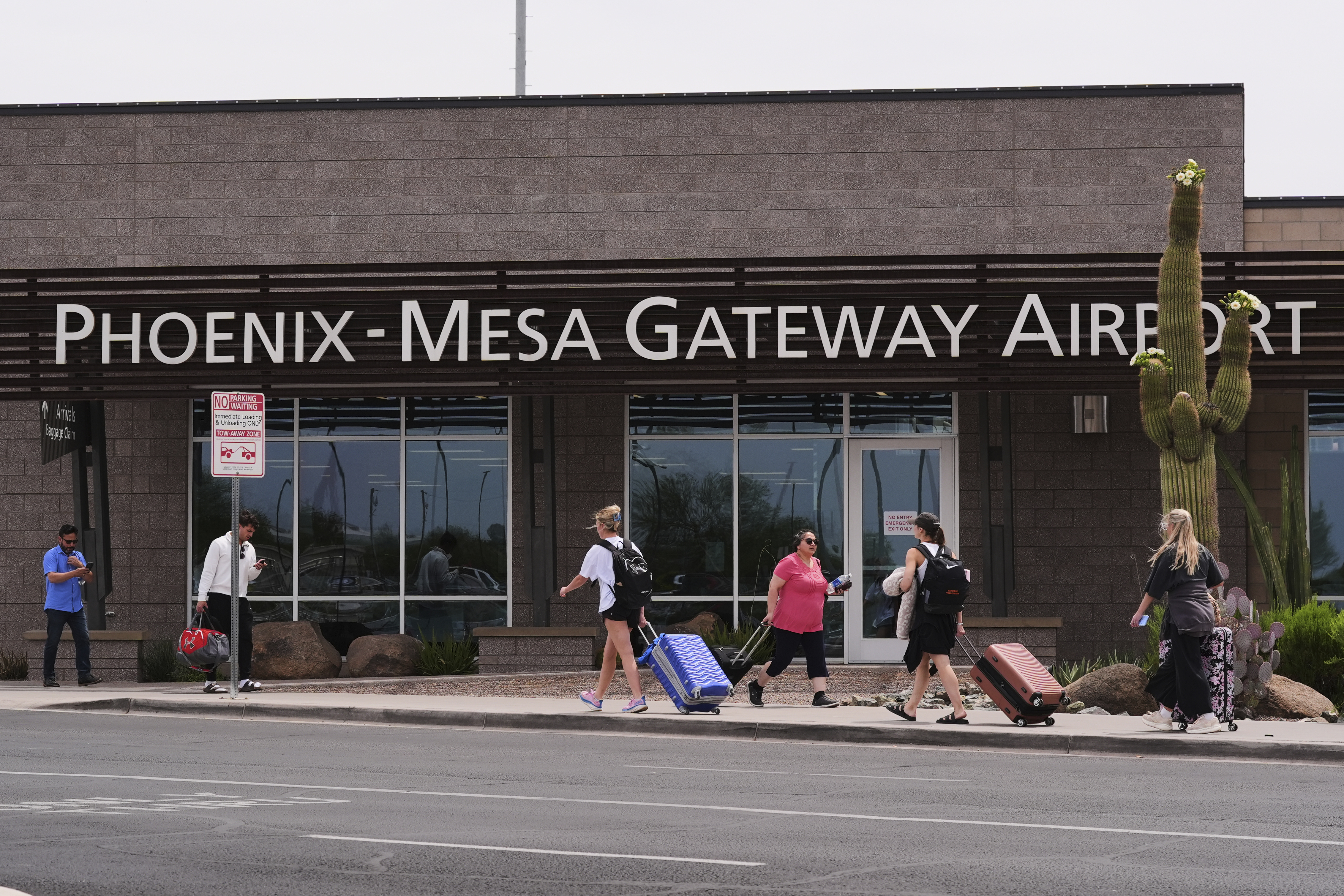 Passengers walk in front of Mesa Gateway Airport, where Avelo Airlines started making deportation flights on behalf of the federal government on Monday, May 12, 2025, in Mesa, Ariz. (AP Photo/Ross D. Franklin)