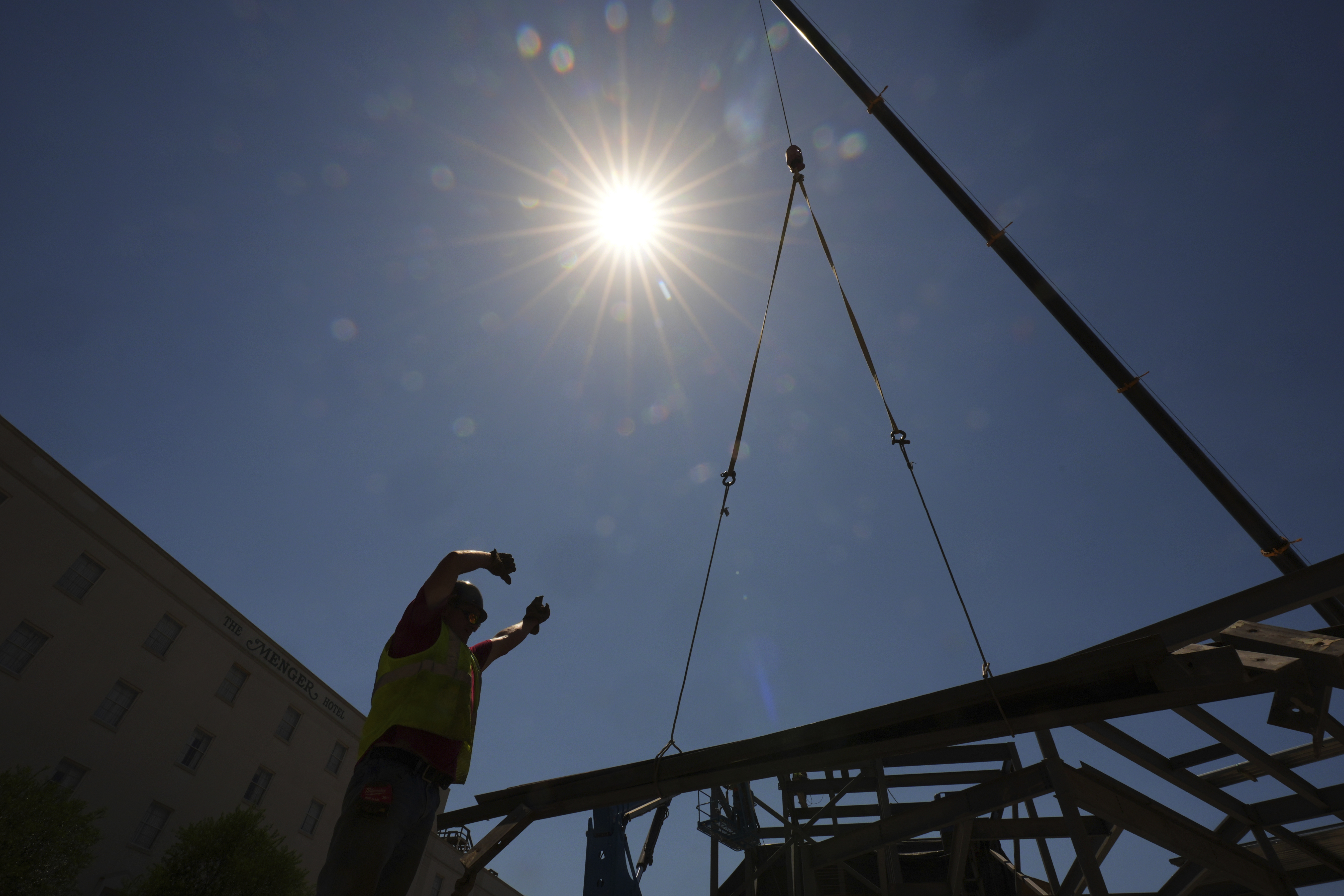A construction worker guides a crane as temperatures top the triple-digit mark, Tuesday, May 13, 2025, in San Antonio. (AP Photo/Eric Gay)