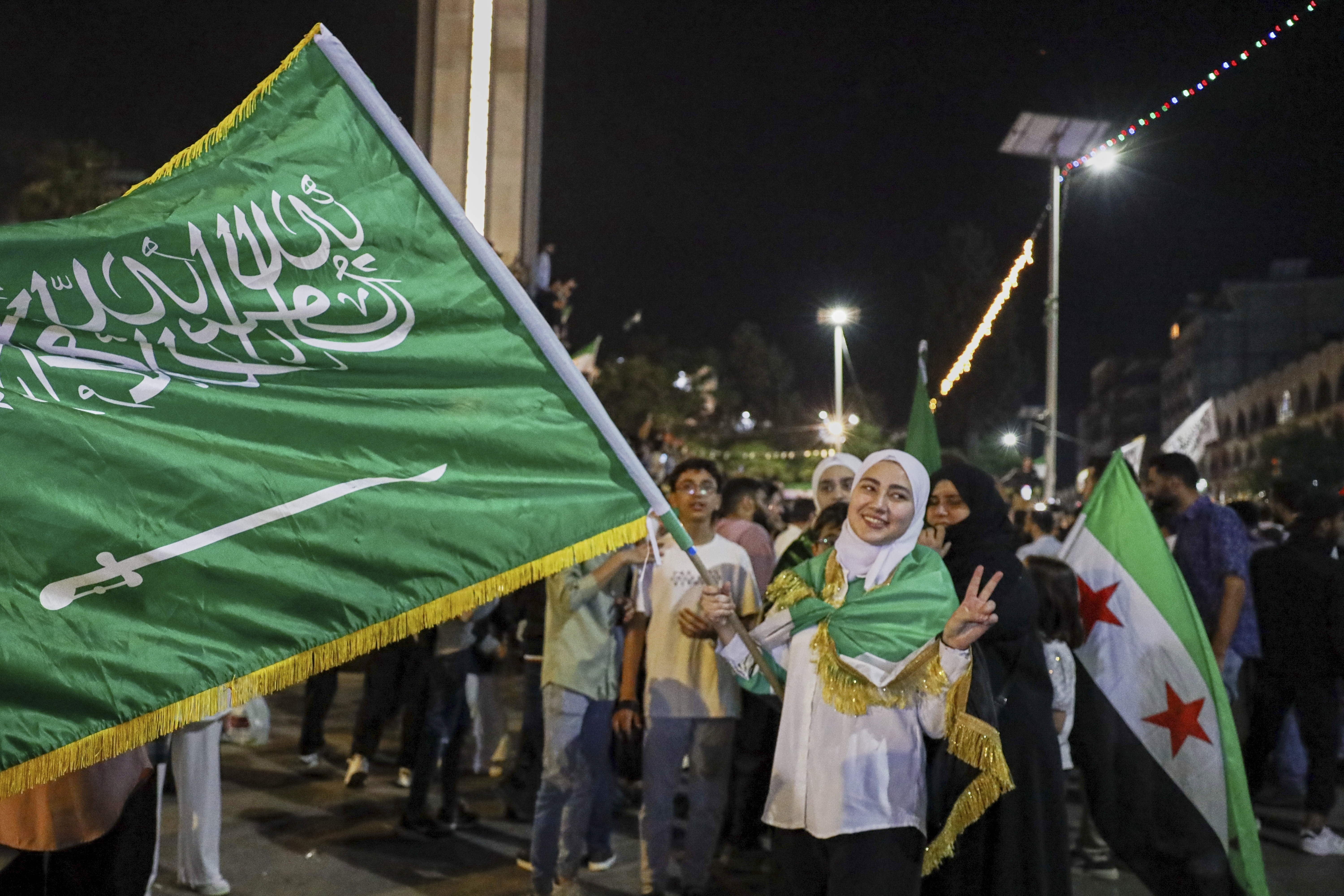 A girl holds a Saudi flag in Homs, Syria, Tuesday, May 13, 2025, as she celebrates U.S. President Donald Trump's plan to ease sanctions on Syria and normalize relations with its new government. Trump made the announcement on a visit to Saudi Arabia. (AP Photo/Omar Albam)