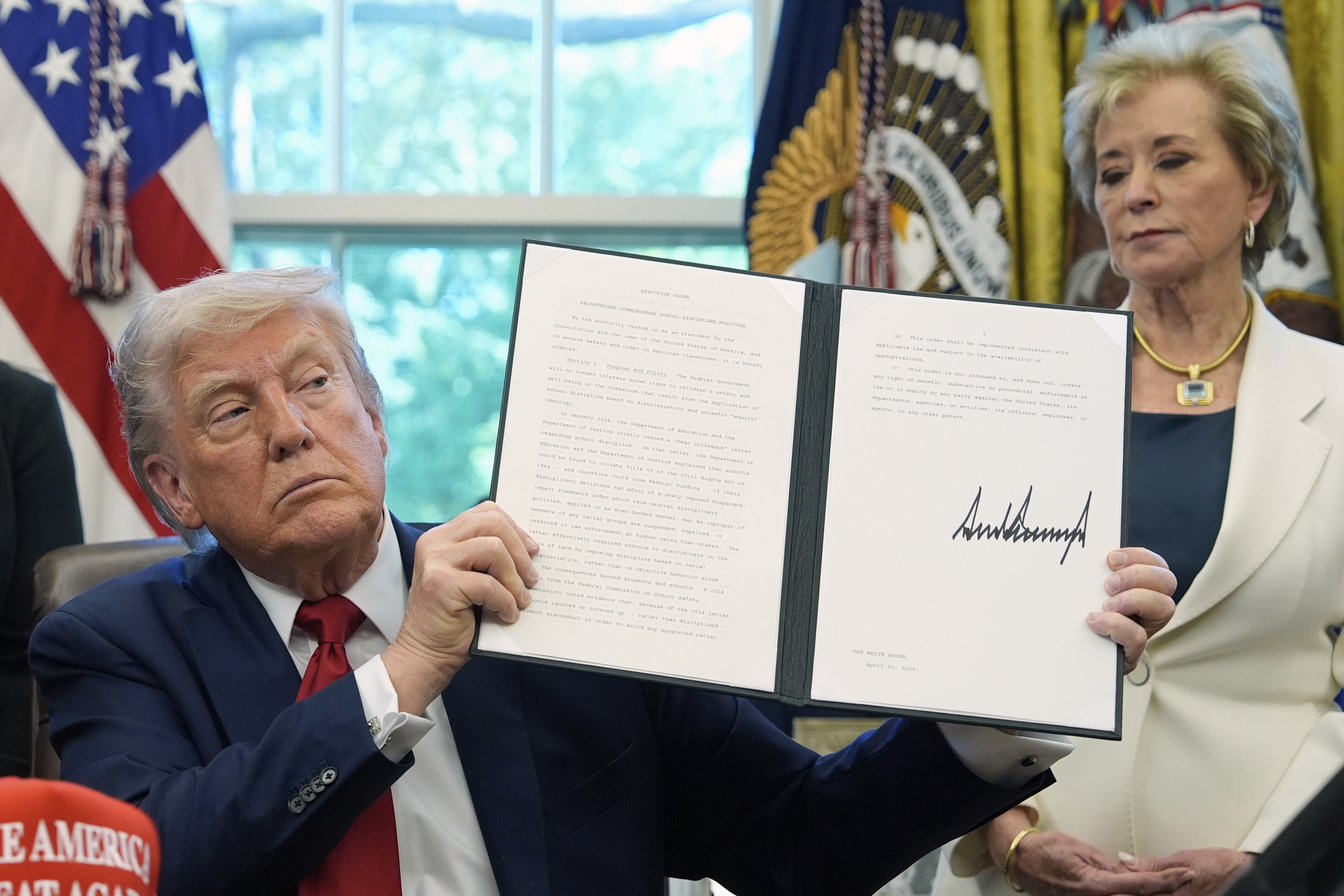 FILE - President Donald Trump holds a signed an executive order relating to school discipline policies as Education Secretary Linda McMahon listens in the Oval Office of the White House, April 23, 2025, in Washington. (AP Photo/Alex Brandon, file)