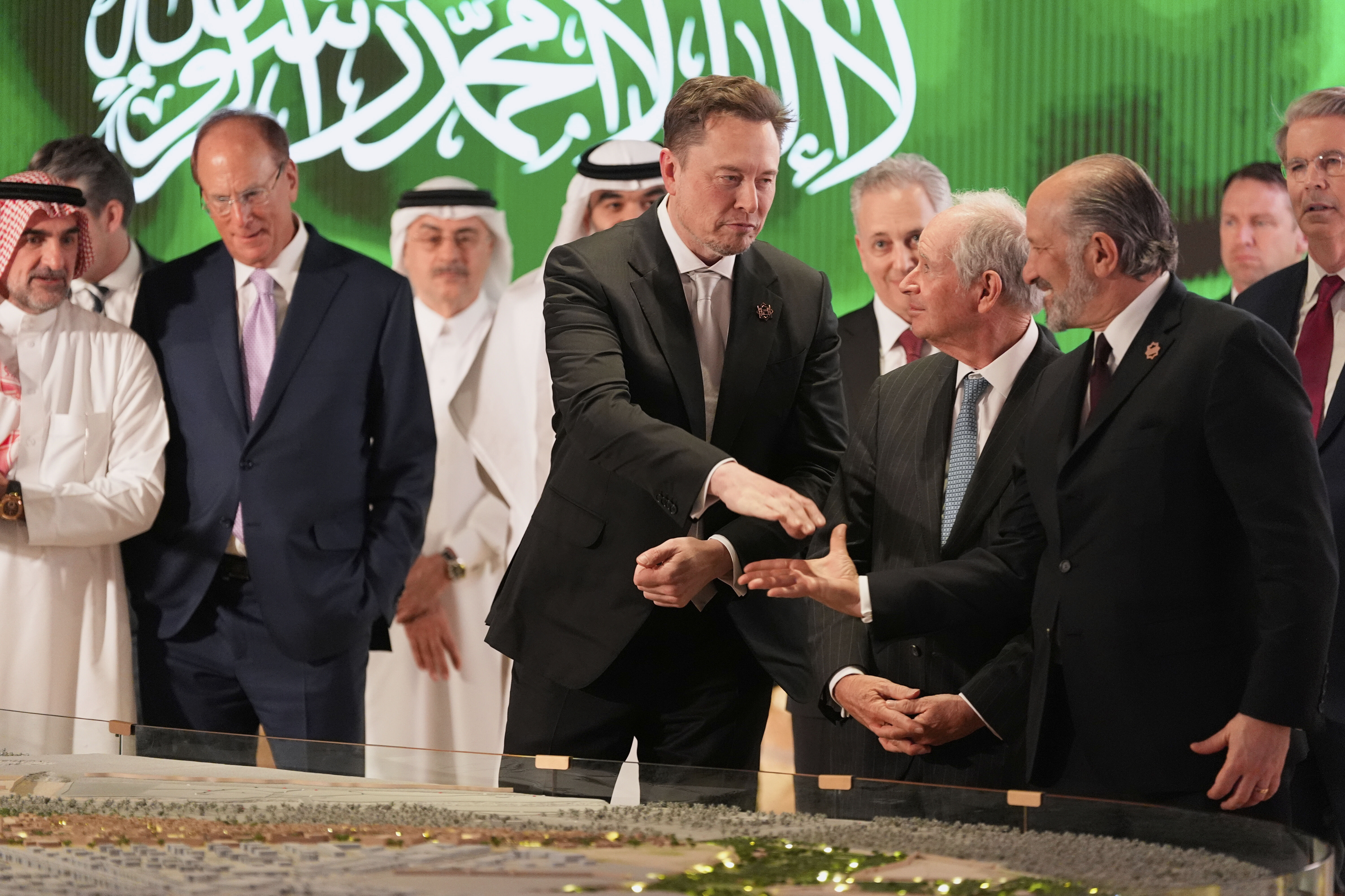 Elon Musk, center, shakes hands with Secretary of Commerce Howard Lutnick, right, as they look at a model of a city under construction, Tuesday, May 13, 2025, in Riyadh, Saudi Arabia. (AP Photo/Alex Brandon)