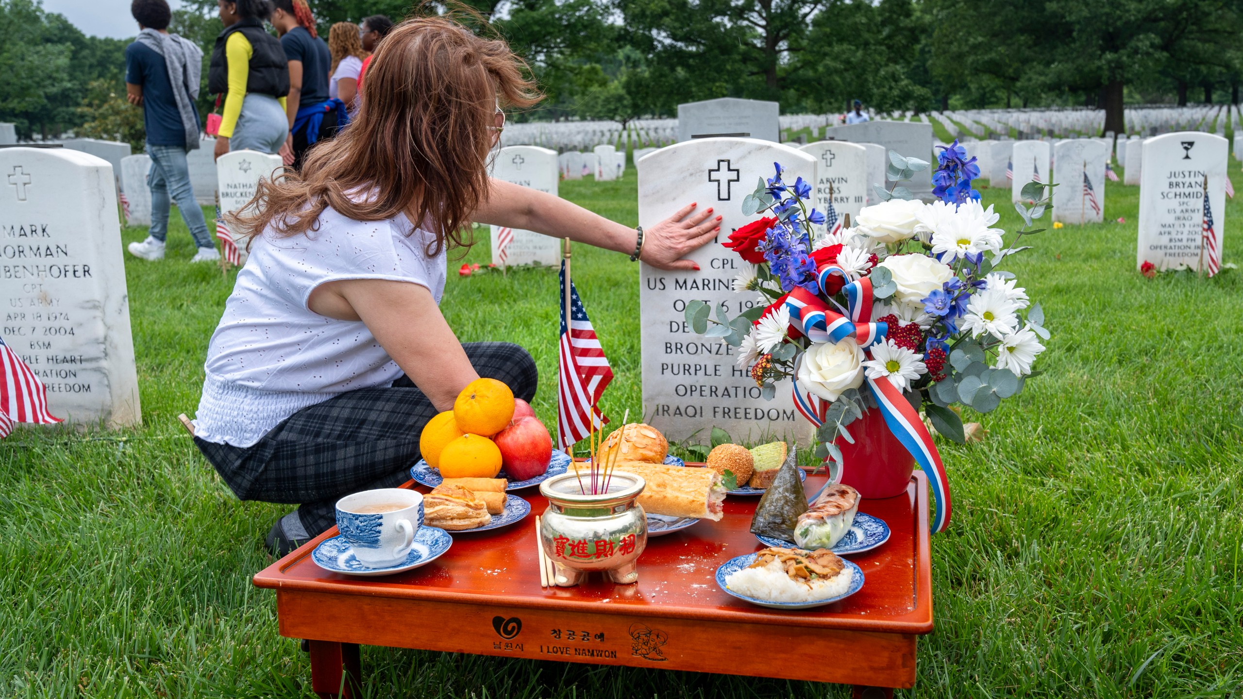FILE - Kim Hoan Nguyen, of Falls Church, Va., who is originally from Vietnam, touches her son's gravestone next to ritual offerings in the Vietnamese tradition at the gravesite of her son, Marine Corporal Binh N Le, who died serving in Iraq in 2004, in Section 60 of Arlington National Cemetery, in Arlington, Va., Monday, May 27, 2024, on Memorial Day. (AP Photo/Jacquelyn Martin, File)