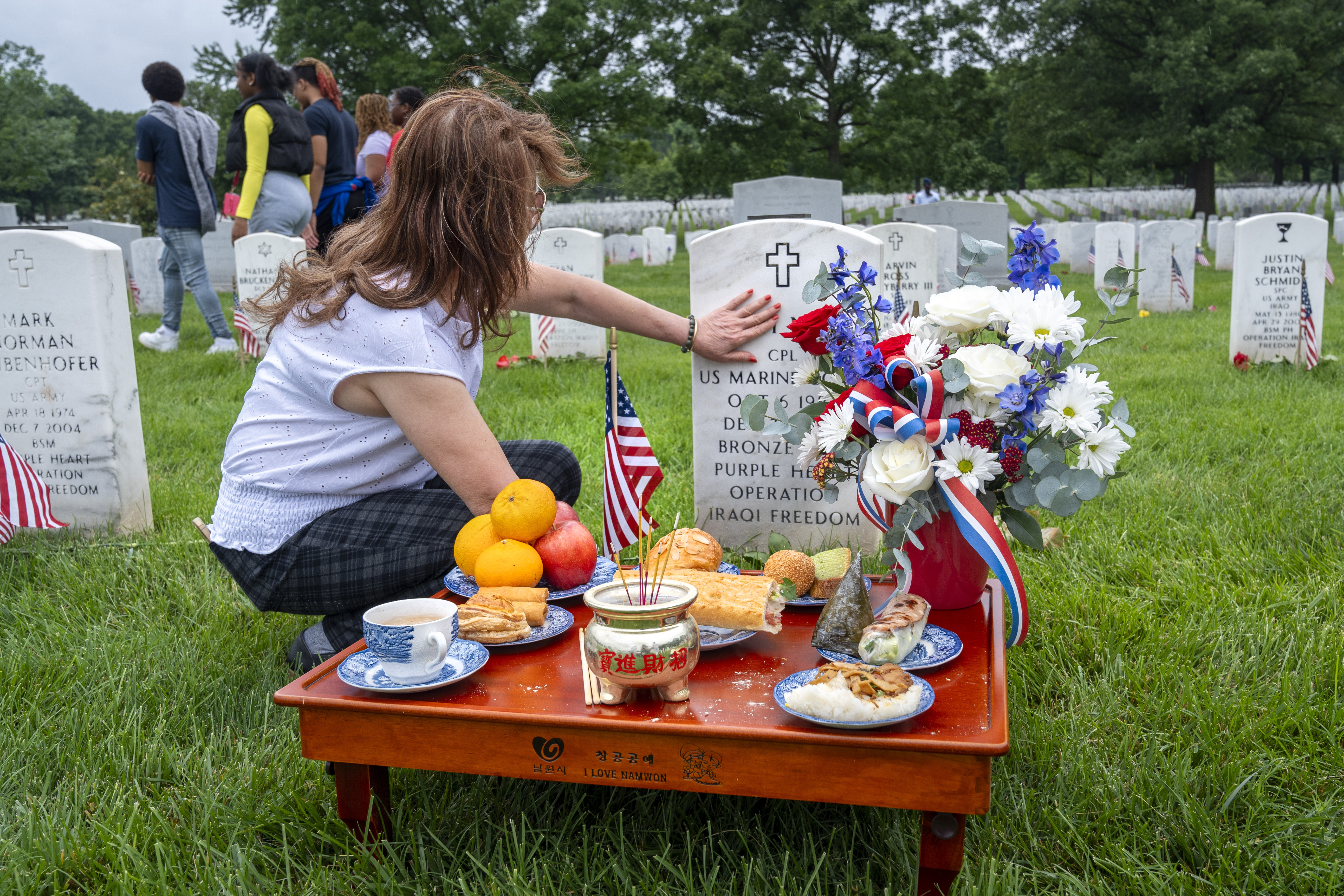FILE - Kim Hoan Nguyen, of Falls Church, Va., who is originally from Vietnam, touches her son's gravestone next to ritual offerings in the Vietnamese tradition at the gravesite of her son, Marine Corporal Binh N Le, who died serving in Iraq in 2004, in Section 60 of Arlington National Cemetery, in Arlington, Va., Monday, May 27, 2024, on Memorial Day. (AP Photo/Jacquelyn Martin, File)
