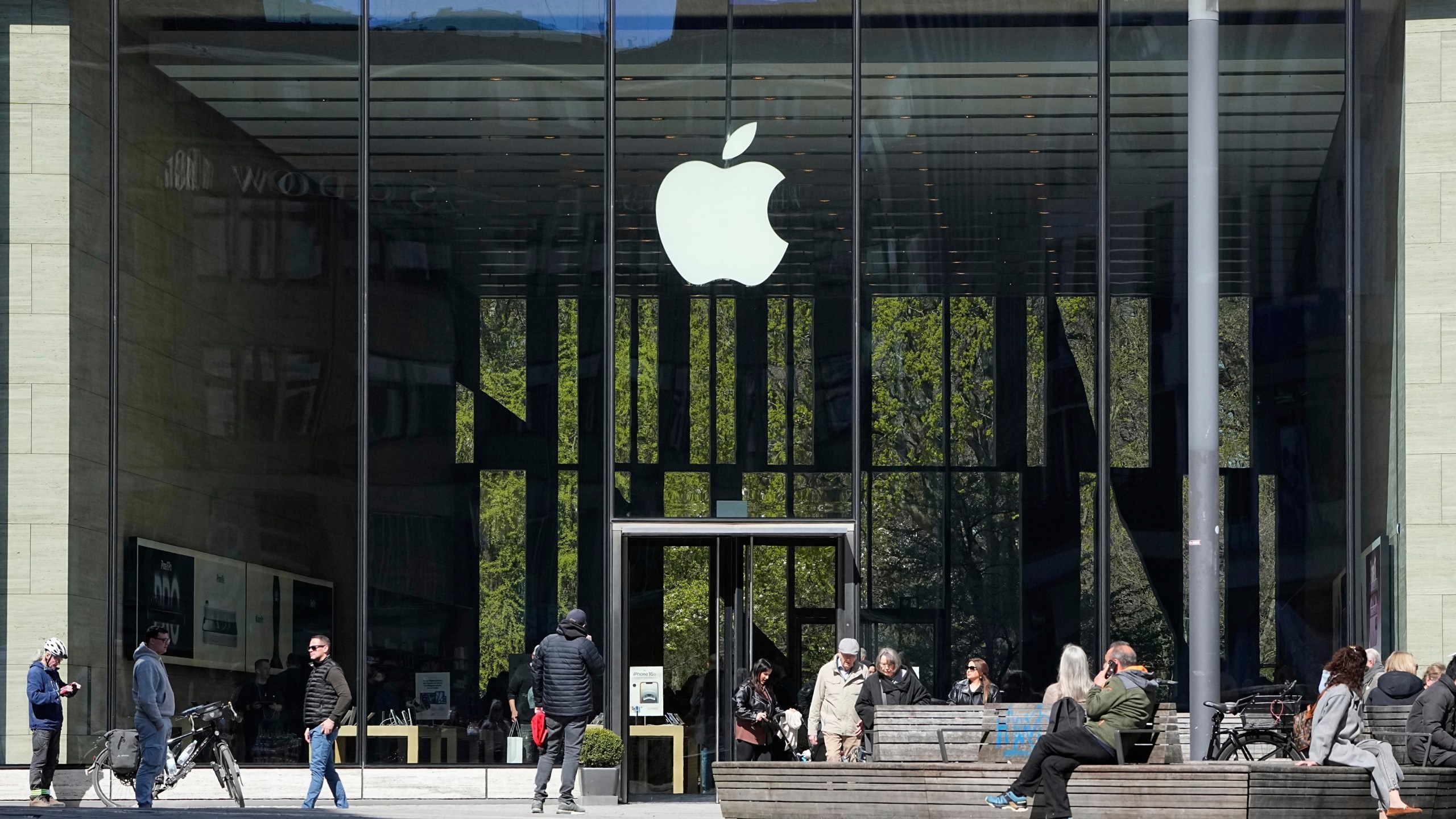 FILE - People sit in front of an Apple Store in Duesseldorf, Germany, Monday, April 7, 2025. (AP Photo/Martin Meissner, File)