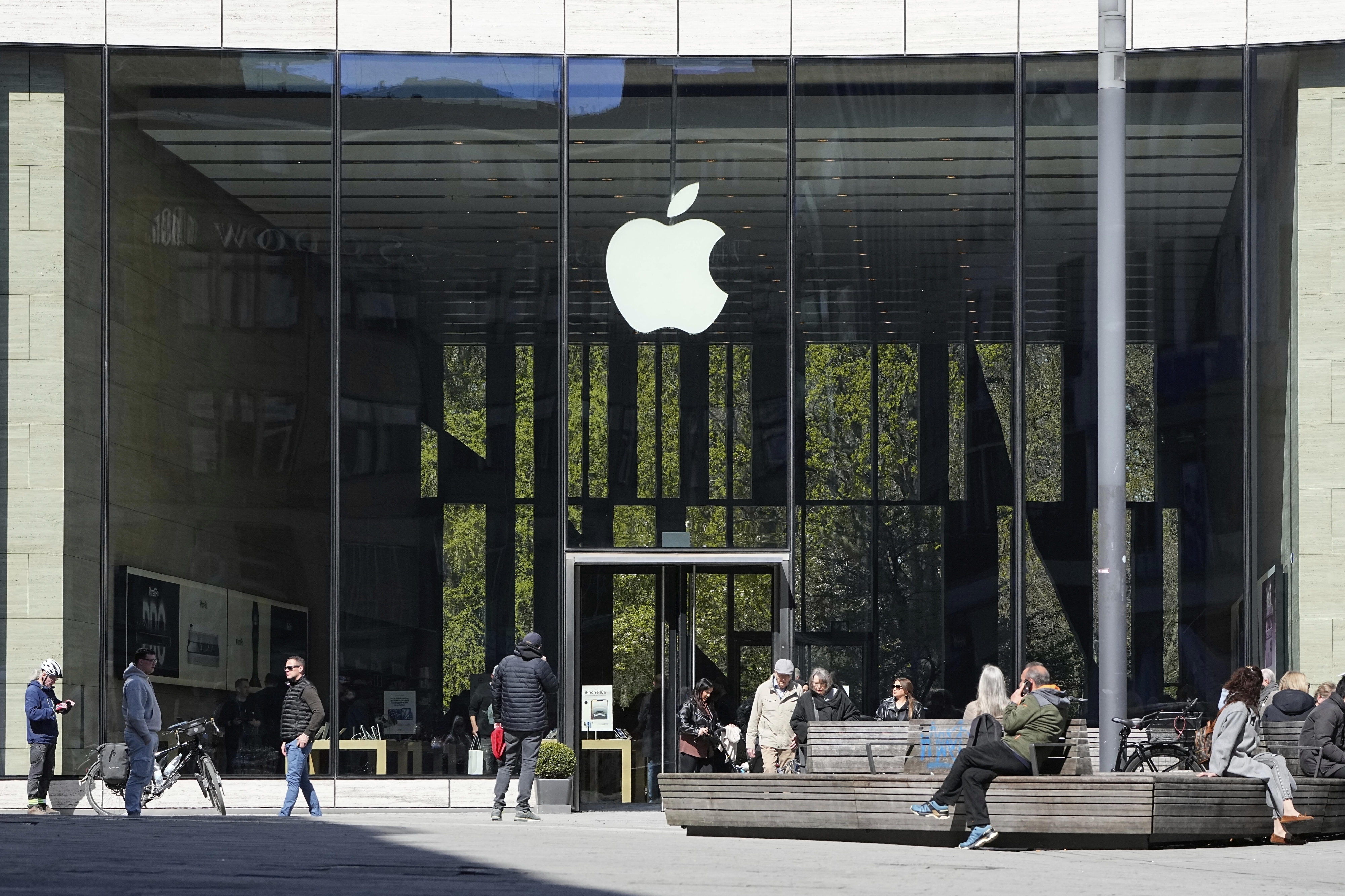 FILE - People sit in front of an Apple Store in Duesseldorf, Germany, Monday, April 7, 2025. (AP Photo/Martin Meissner, File)