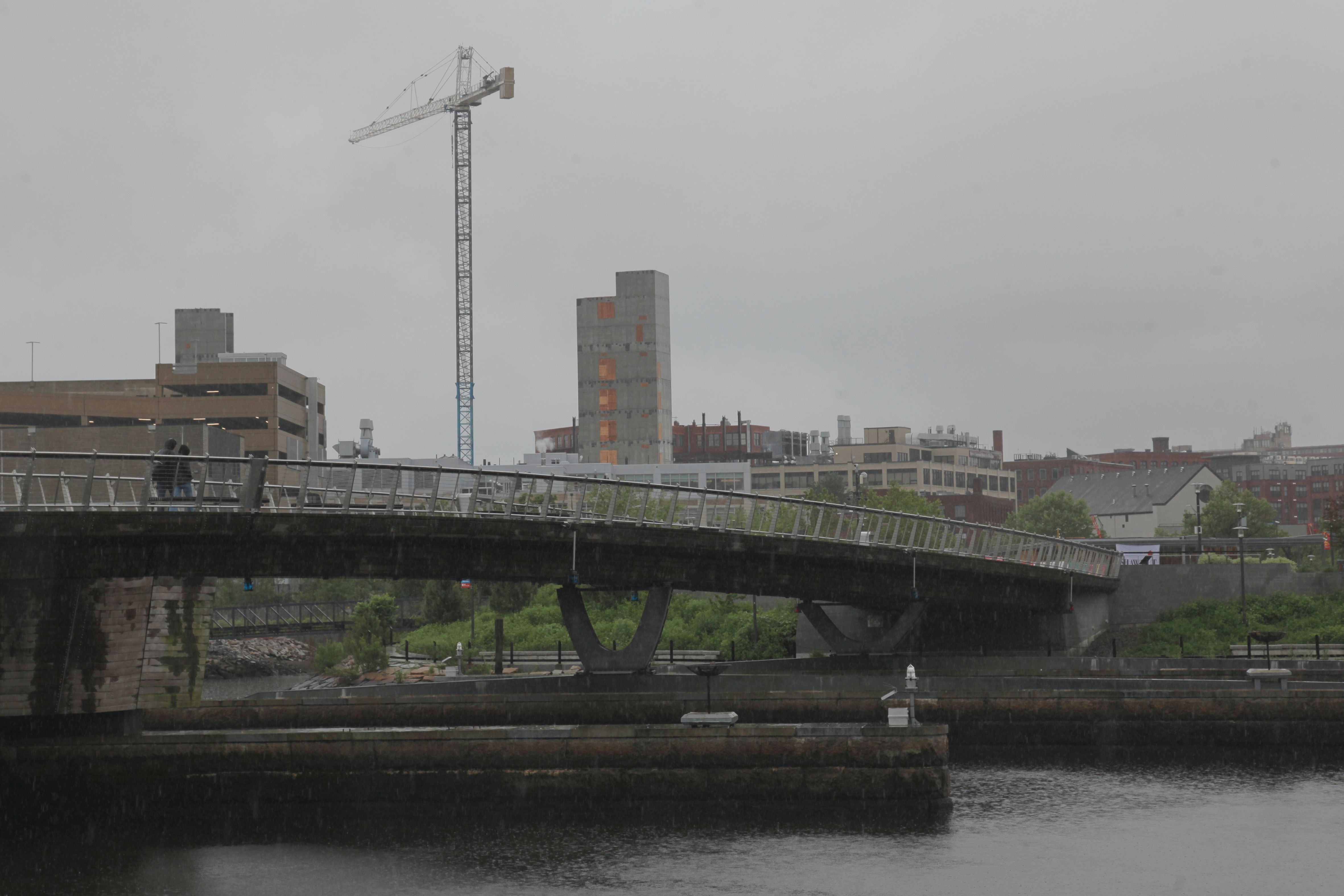 A man walks in the rain across a pedestrian bridge in Providence, R.I. on Thursday, May 22, 2025. (AP Photo/Kimberlee Kruesi)
