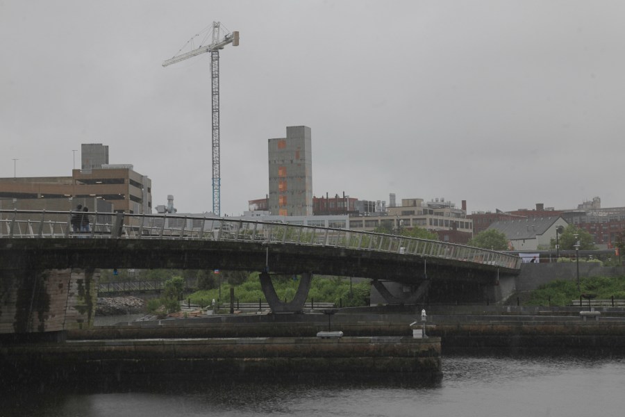 A man walks in the rain across a pedestrian bridge in Providence, R.I. on Thursday, May 22, 2025. (AP Photo/Kimberlee Kruesi)
