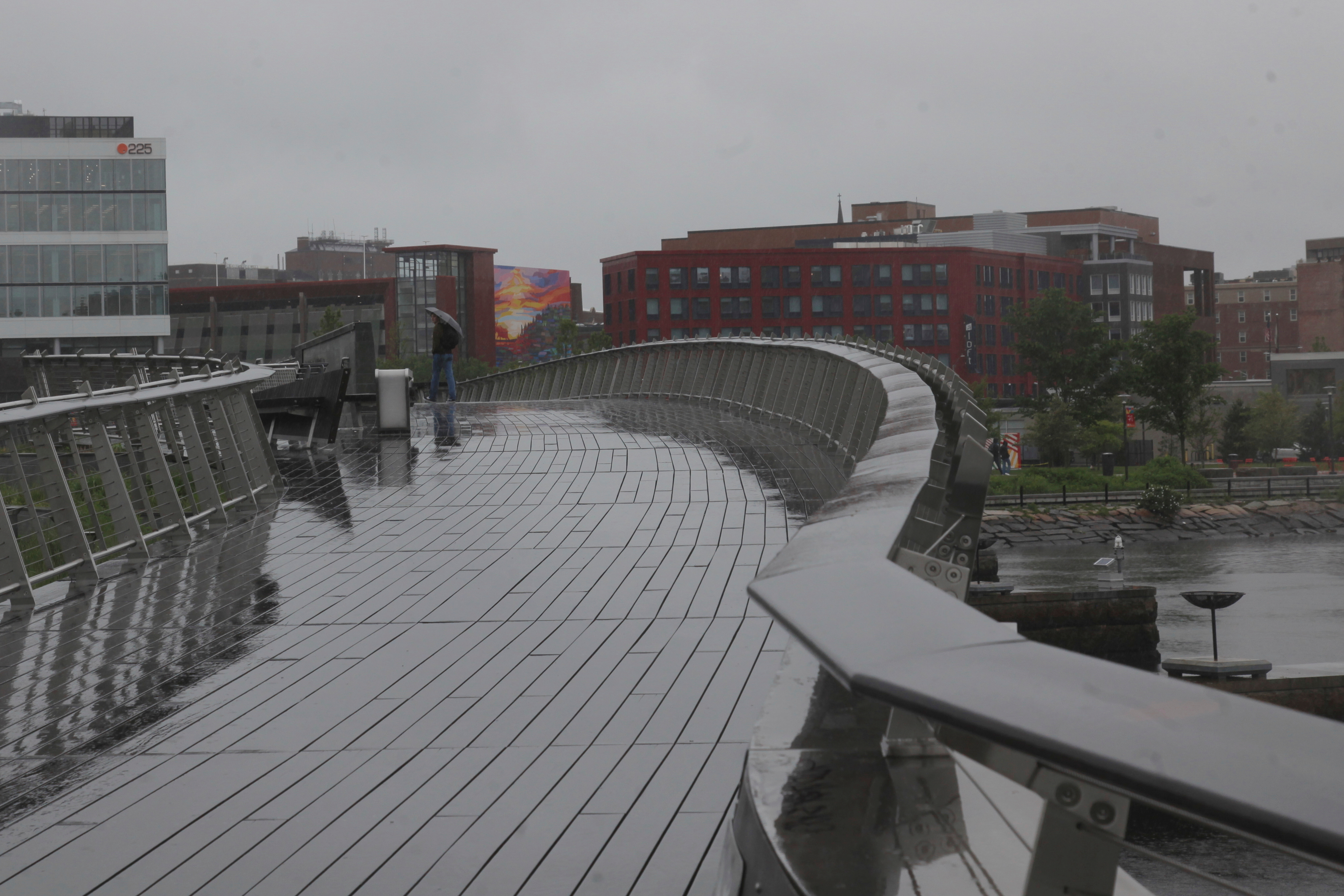 A man walks in the rain across a pedestrian bridge in Providence, R.I. (AP Photo/Kimberlee Kruesi)