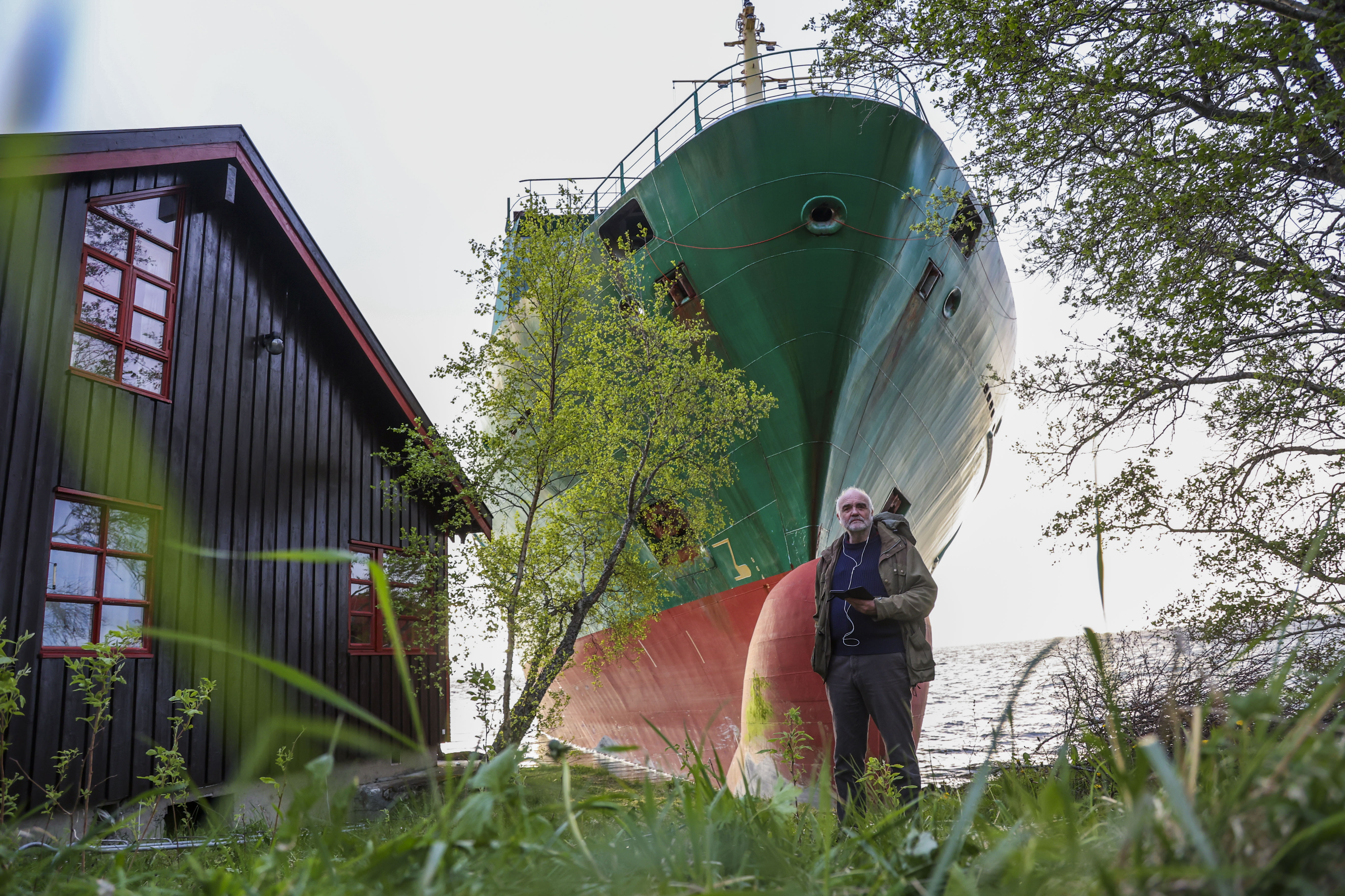 Johan Helberg stands next to his house, with the container ship NCL Salten in the background, after the 135-meter-long ship ran aground in the Trondheimsfjord, outside Byneset, in Trondheim, Norway, Thursday May 22, 2025. (Jan Langhaug/NTB Scanpix via AP)