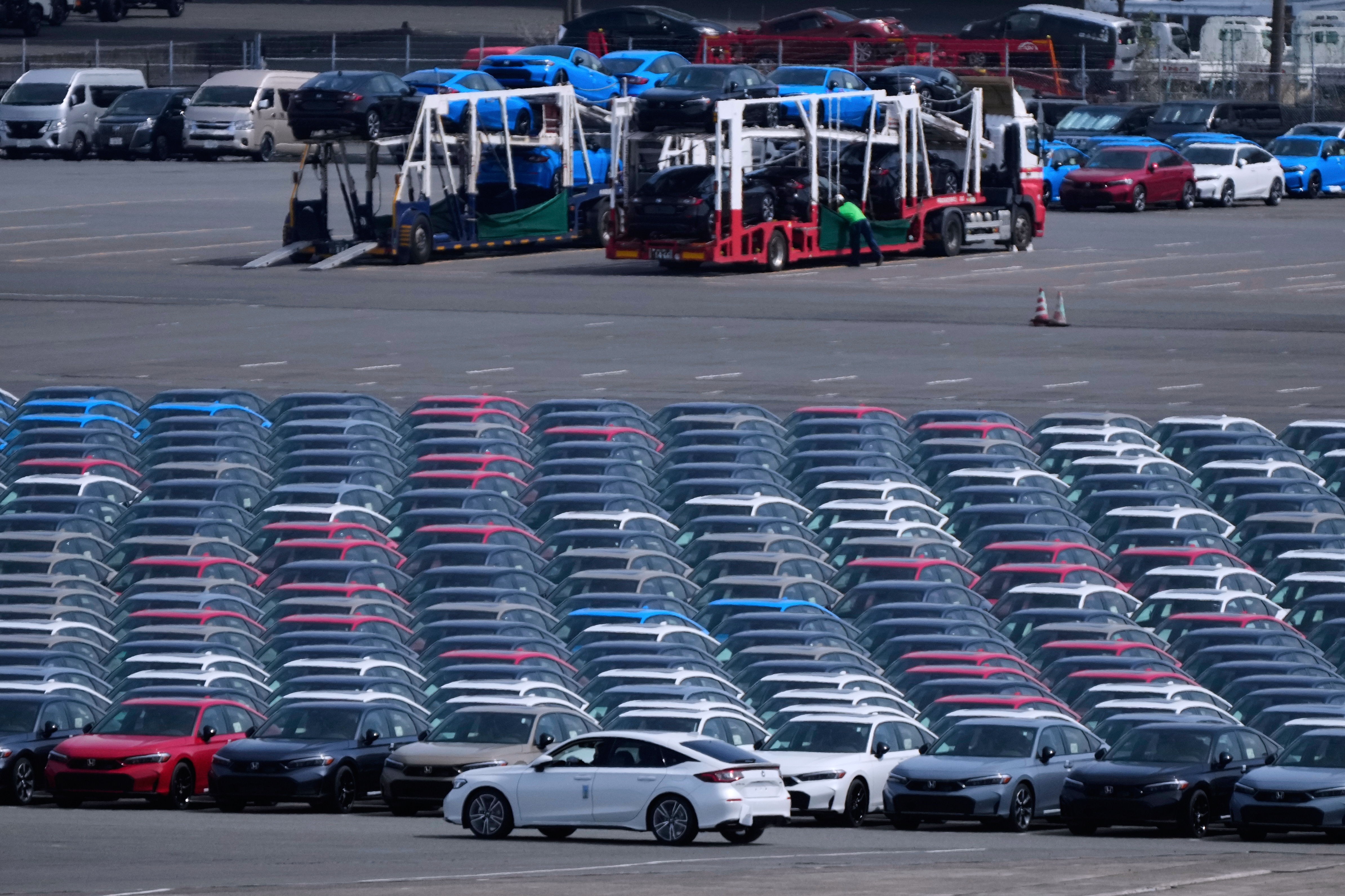 FILE - Workers, back, unload vehicles while a car, center front, is moved to another location of the area, where export vehicles are parked at the Daikoku vehicle terminal center in Yokohama, near Tokyo, April 8, 2025. (AP Photo/Hiro Komae, File)