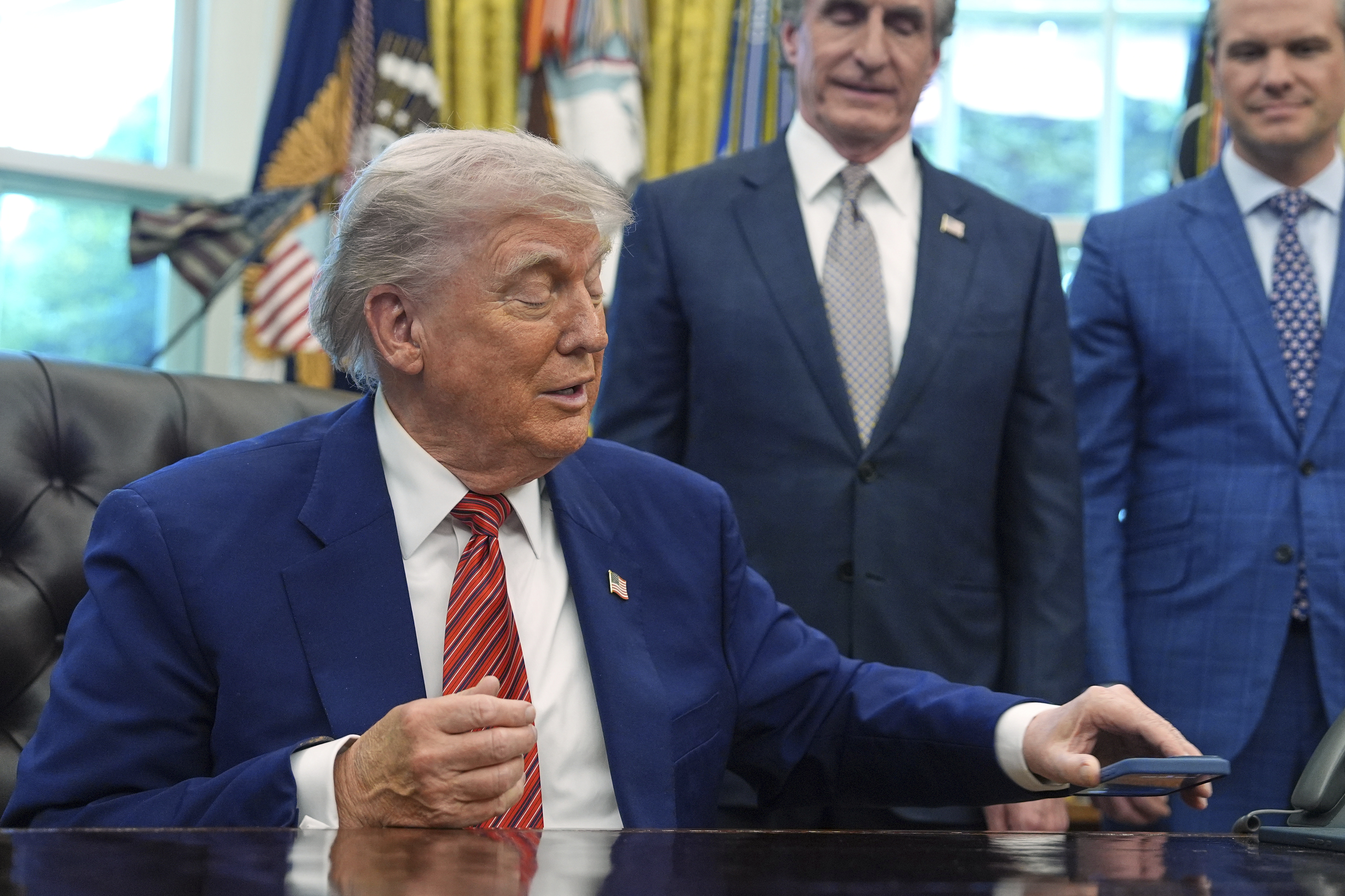 President Donald Trump silences his mobile phone which rang two times as he was speaking to reporters after signing executive orders regarding nuclear energy in the Oval Office of the White House, Friday, May 23, 2025, in Washington. (AP Photo/Evan Vucci)