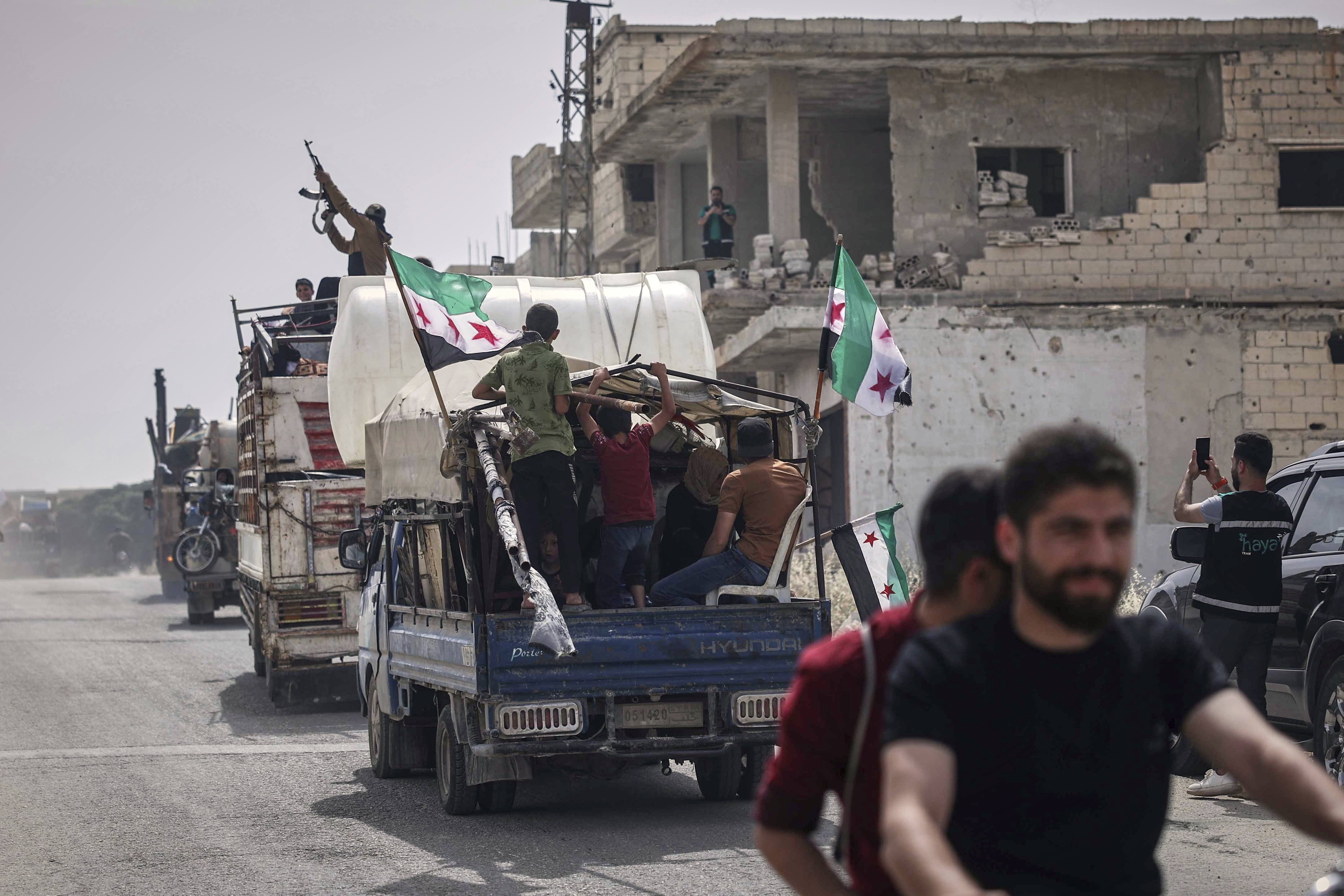 A man fires into the air from one of the trucks carrying some of the 60 displaced families who, supported by an NGO, are returning to their village after more than five years in the Atmeh camps near the Syrian-Turkish border, in Kafr Sijna, south of Idlib, Syria, Sunday, May 18, 2025. (AP Photo/Ghaith Alsayed)