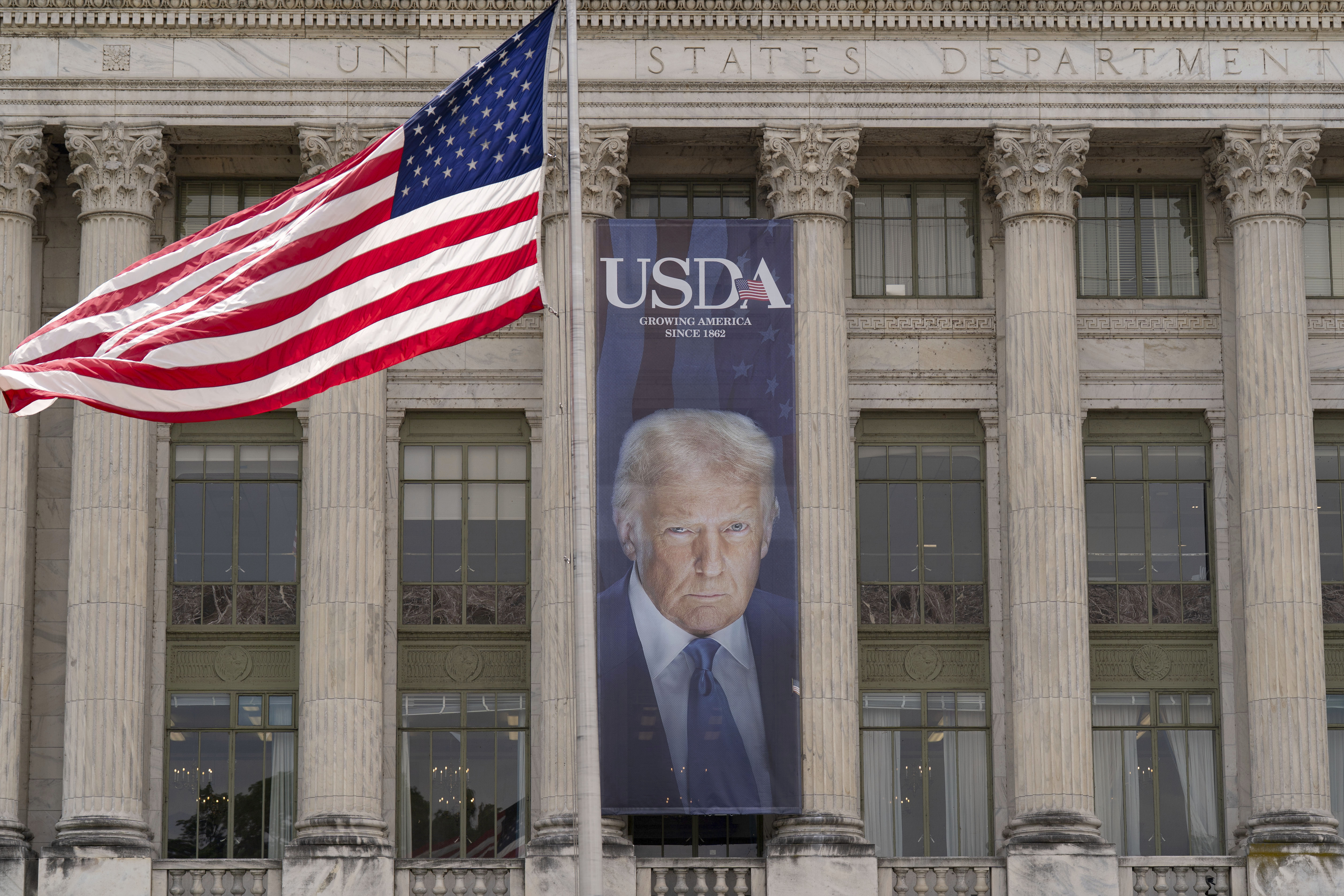 A banner with a photograph of President Donald Trump hangs near the entrance of the U.S. Department of Agriculture building in Washington, Friday, May 16, 2025. (AP Photo/Jose Luis Magana)