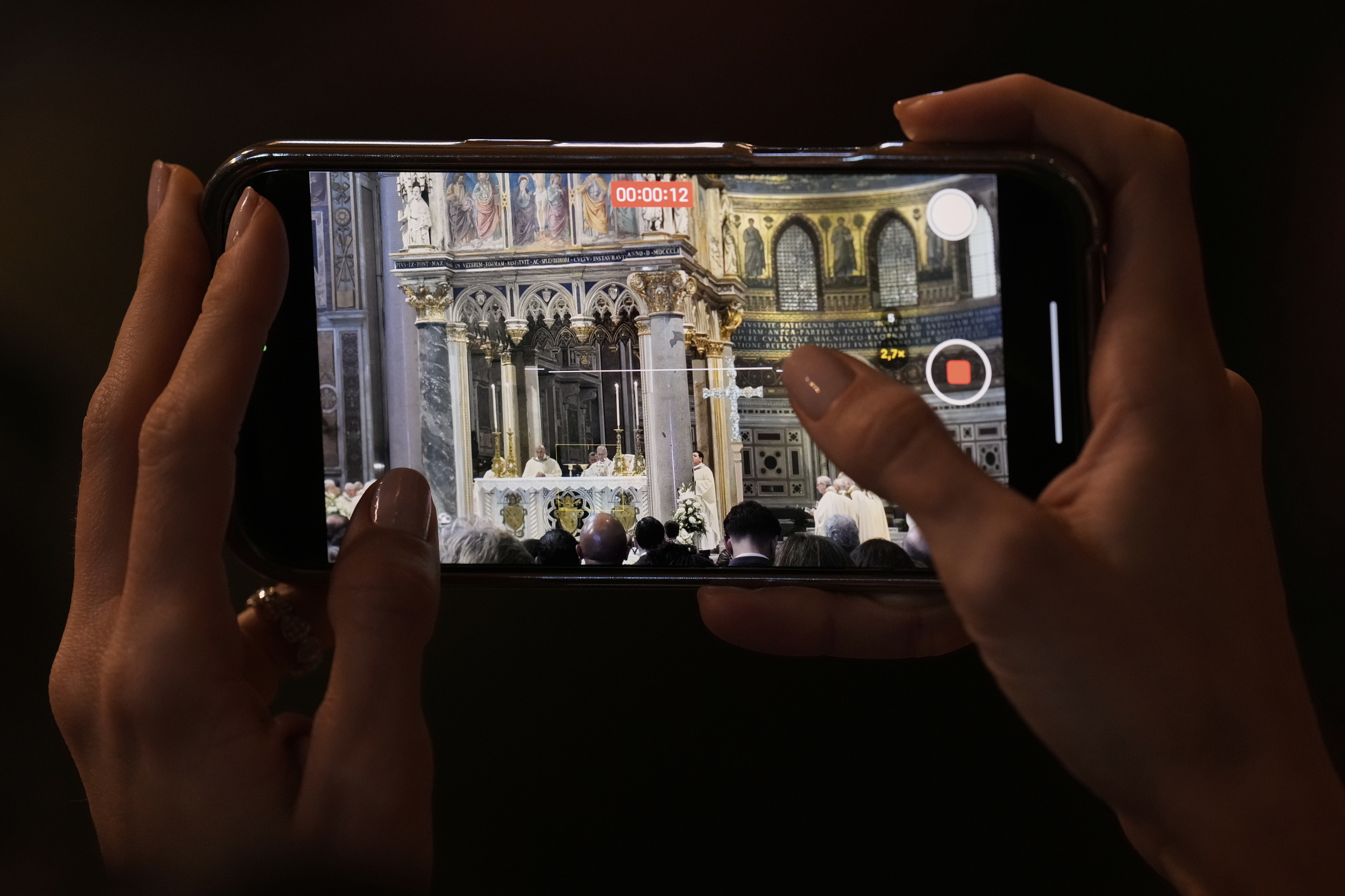 A woman takes photos with her phone to Pope Leo XIV presides over a Mass in the Archbasilica of St. John Lateran and takes possession of the Roman Cathedra, formalising his role as Bishop of Rome in Rome, Sunday, May 25, 2025. (AP Photo/Gregorio Borgia)