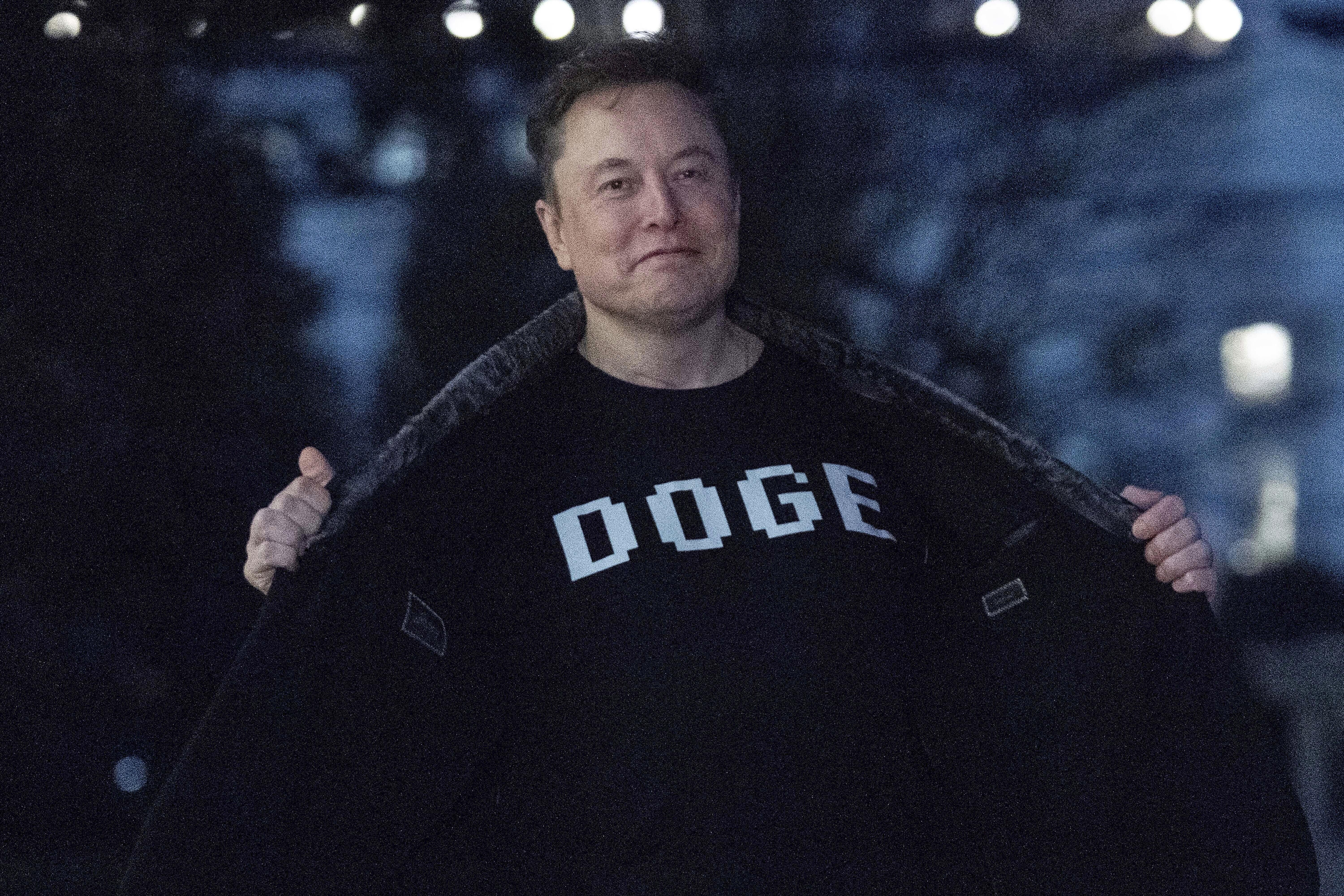 Elon Musk flashes his t-shirt that reads "DOGE" to the media as he walks on South Lawn of the White House, in Washington, Sunday, March 9, 2025. (AP Photo/Jose Luis Magana)