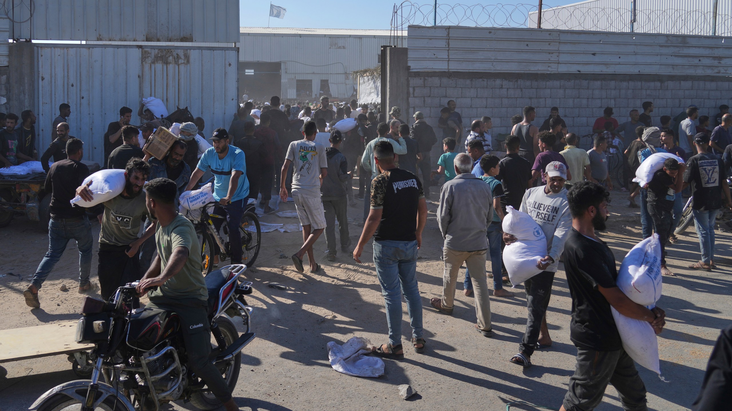 Palestinians carry bags of flour after storming a U.N. World Food Program warehouse in Zawaida, Central Gaza Strip, on Wednesday, May 28, 2025. (AP Photo/Abdel Kareem Hana)