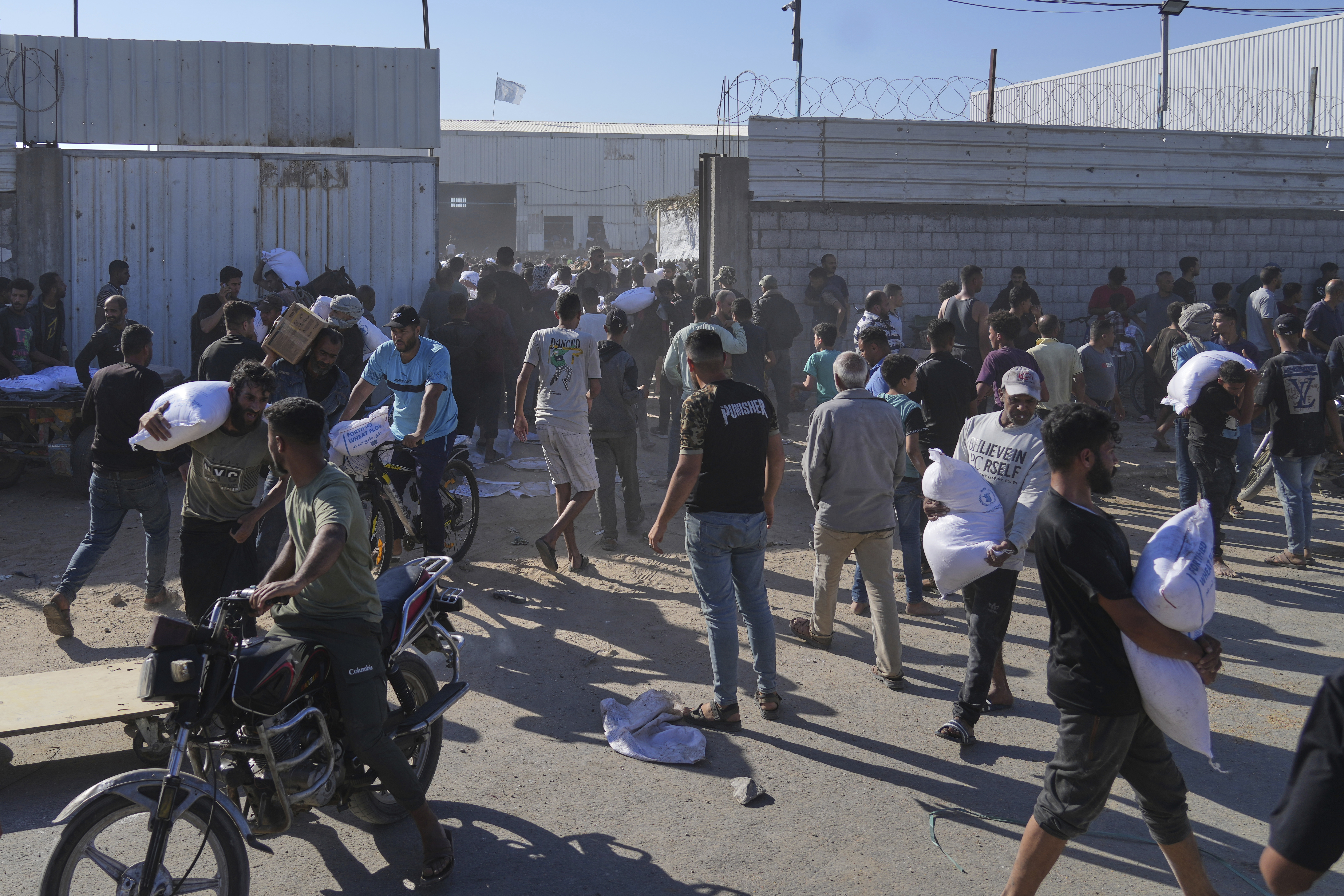 Palestinians carry bags of flour after storming a U.N. World Food Program warehouse in Zawaida, Central Gaza Strip, on Wednesday, May 28, 2025. (AP Photo/Abdel Kareem Hana)