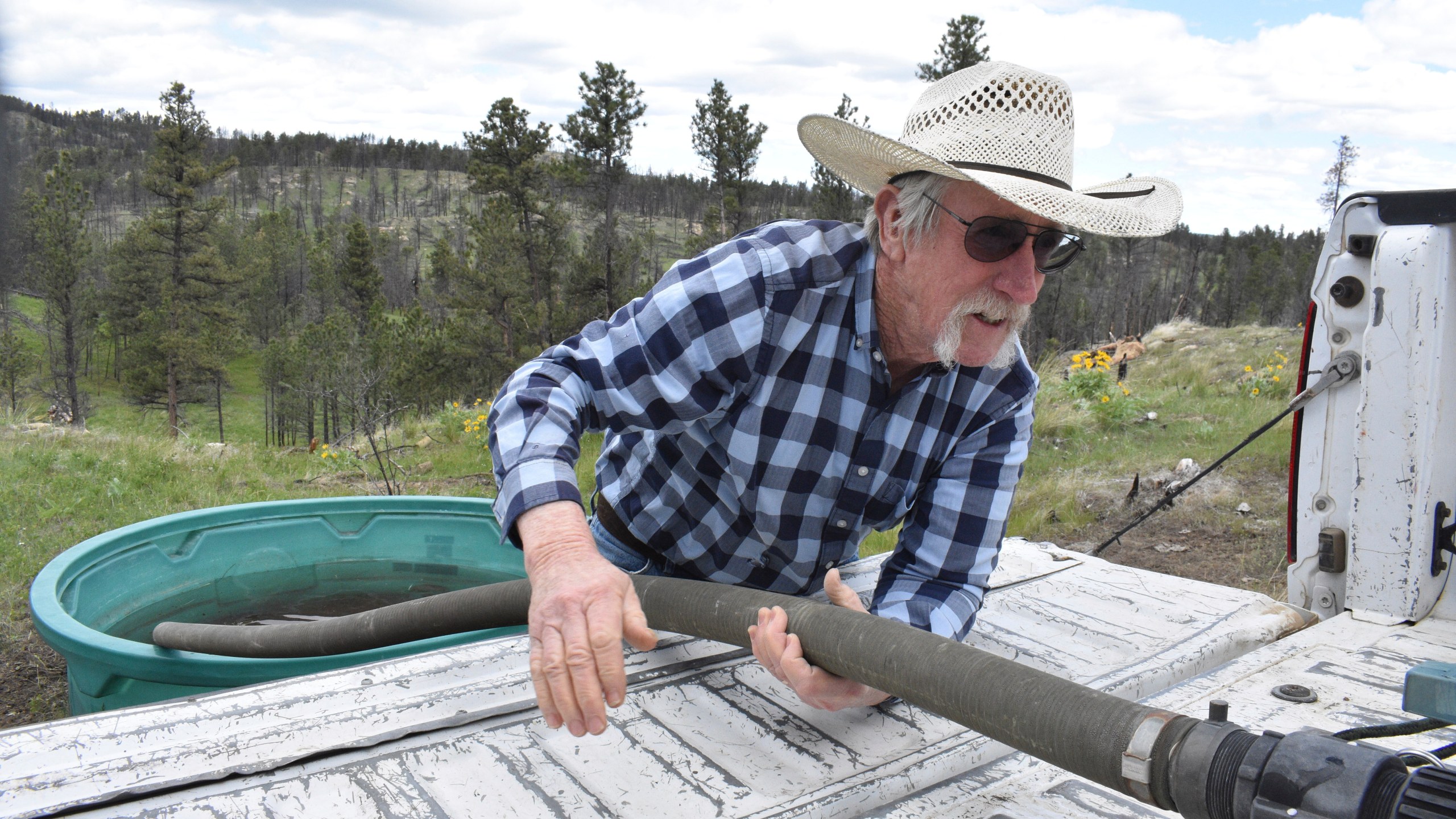 Pat Thiele connects a hose to a water tank as he fills a trough used by his cattle in the Bull Mountains, on May 21, 2025, near Roundup, Montana. (AP Photo/Matthew Brown)