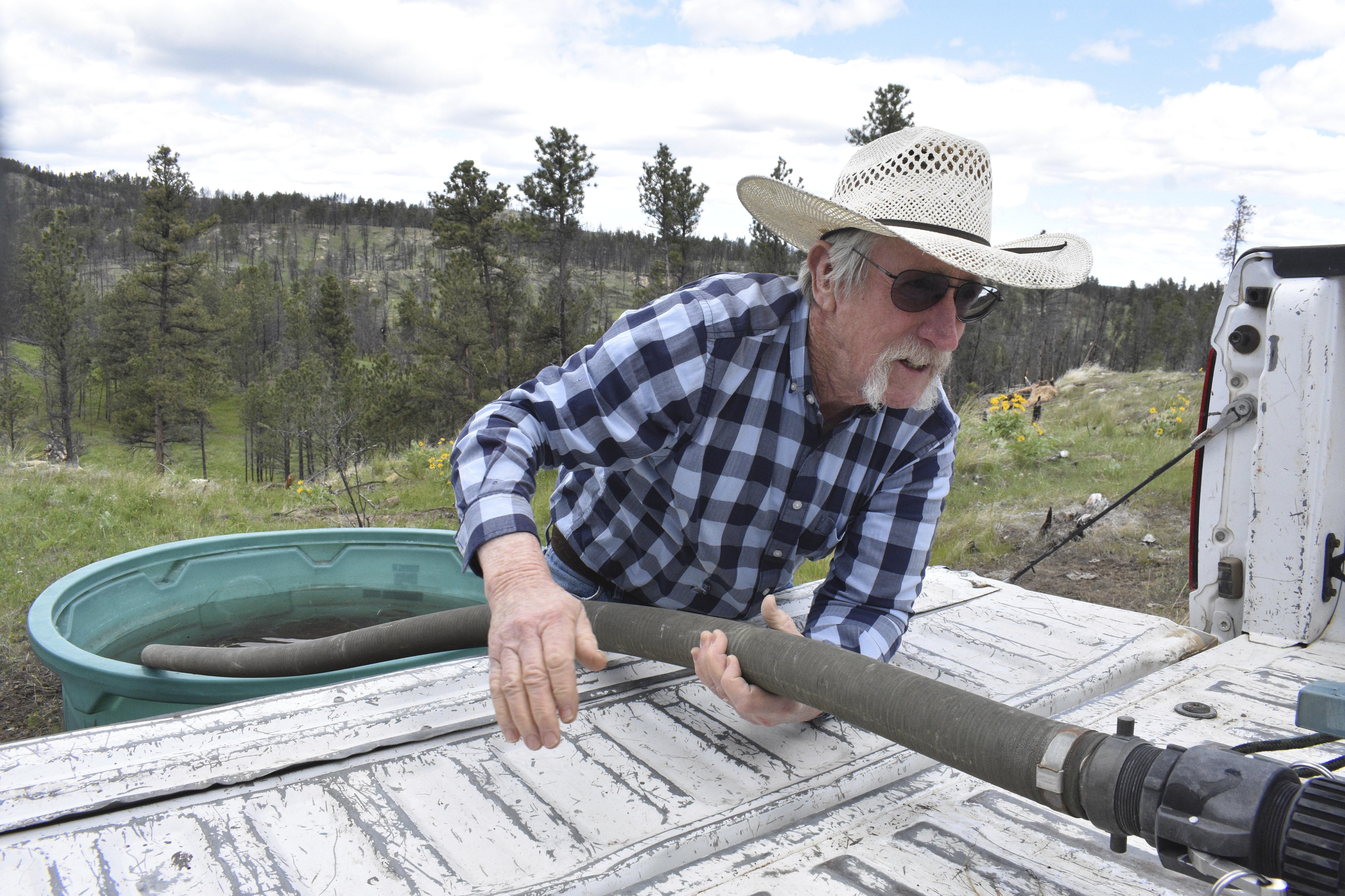 Pat Thiele connects a hose to a water tank as he fills a trough used by his cattle in the Bull Mountains, on May 21, 2025, near Roundup, Montana. (AP Photo/Matthew Brown)
