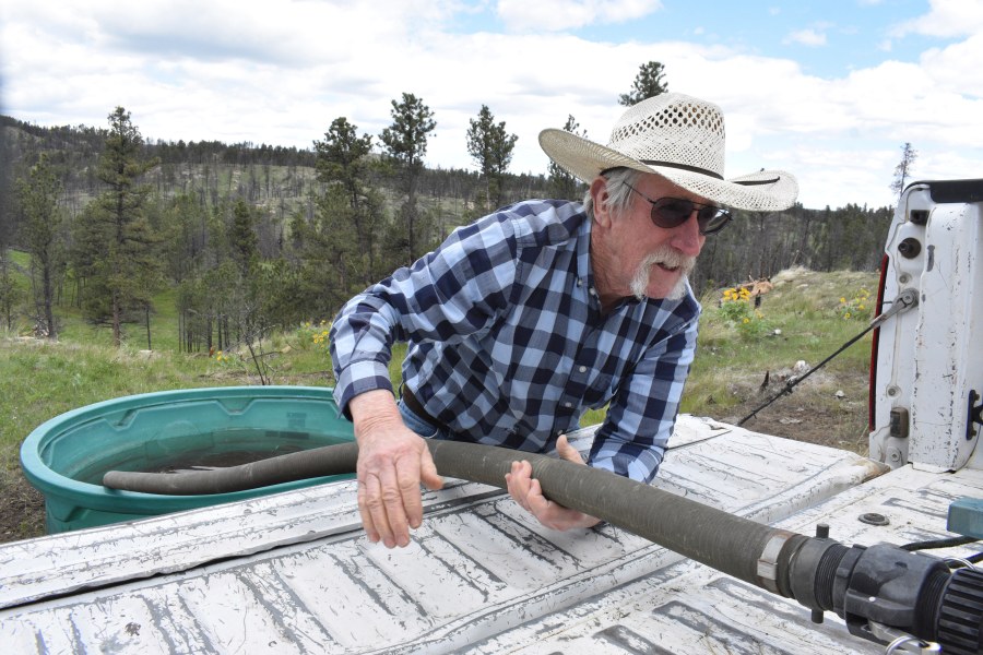 Pat Thiele connects a hose to a water tank as he fills a trough used by his cattle in the Bull Mountains, on May 21, 2025, near Roundup, Montana. (AP Photo/Matthew Brown)